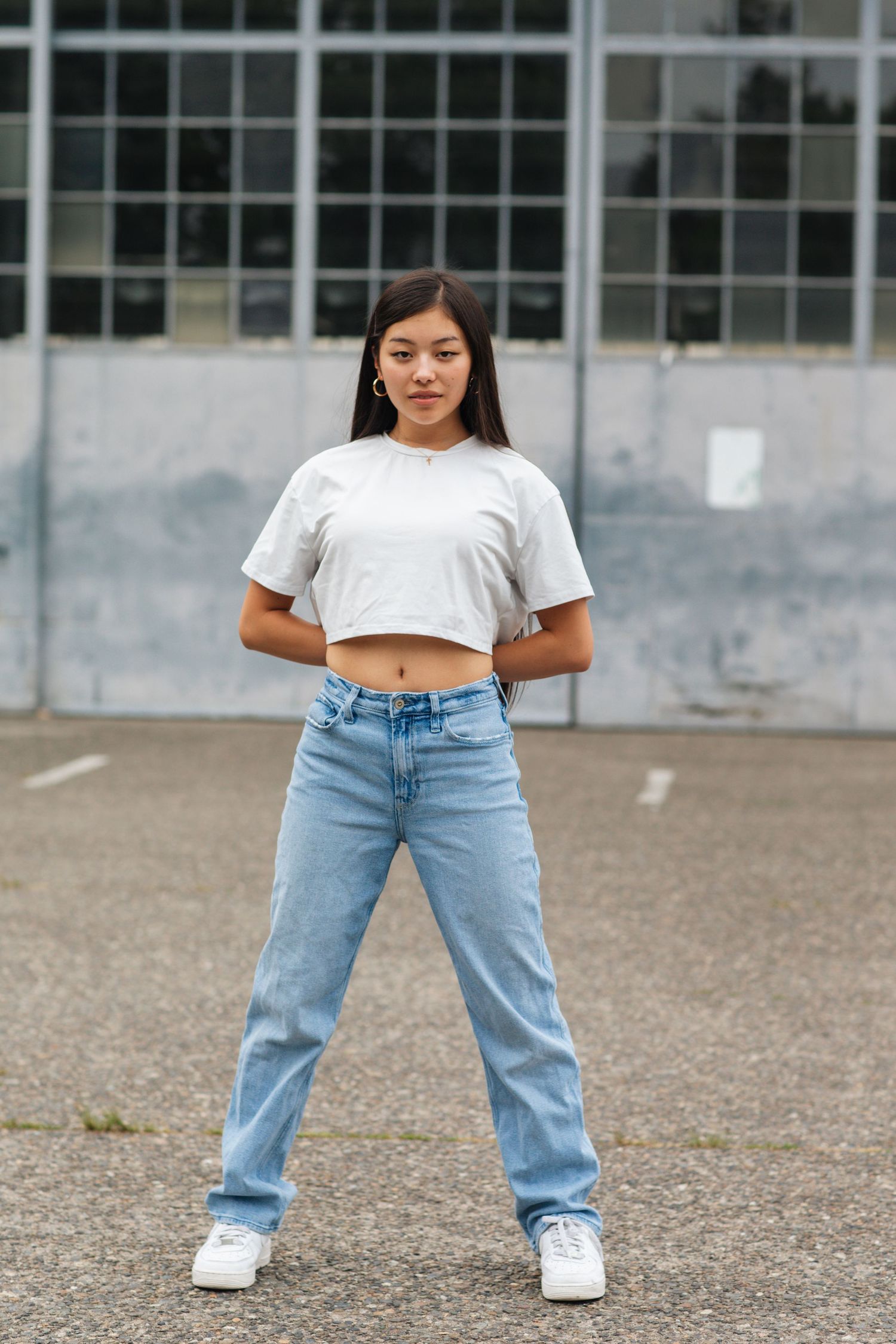 Young woman in white crop top and wide-leg jeans standing confidently in urban outdoor setting.