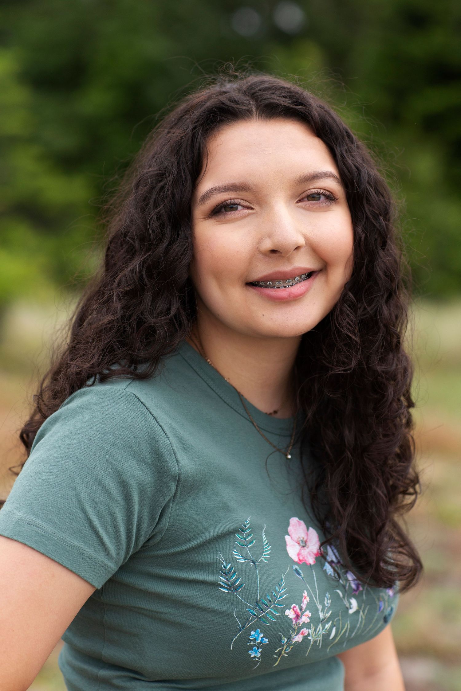 Portrait of smiling teenage girl with braces and curly hair in green floral t-shirt.