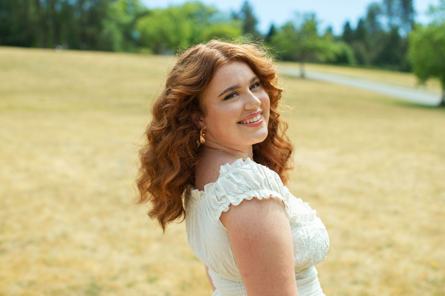 Young woman with red curly hair smiling in golden field.