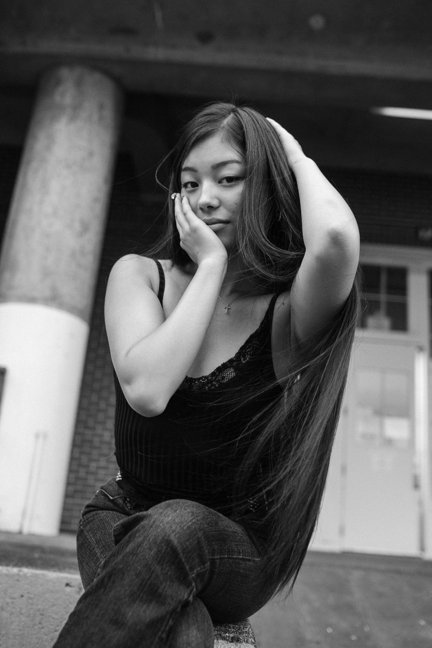 Young woman with long dark hair resting face in hand sitting outdoors in black and white portrait.