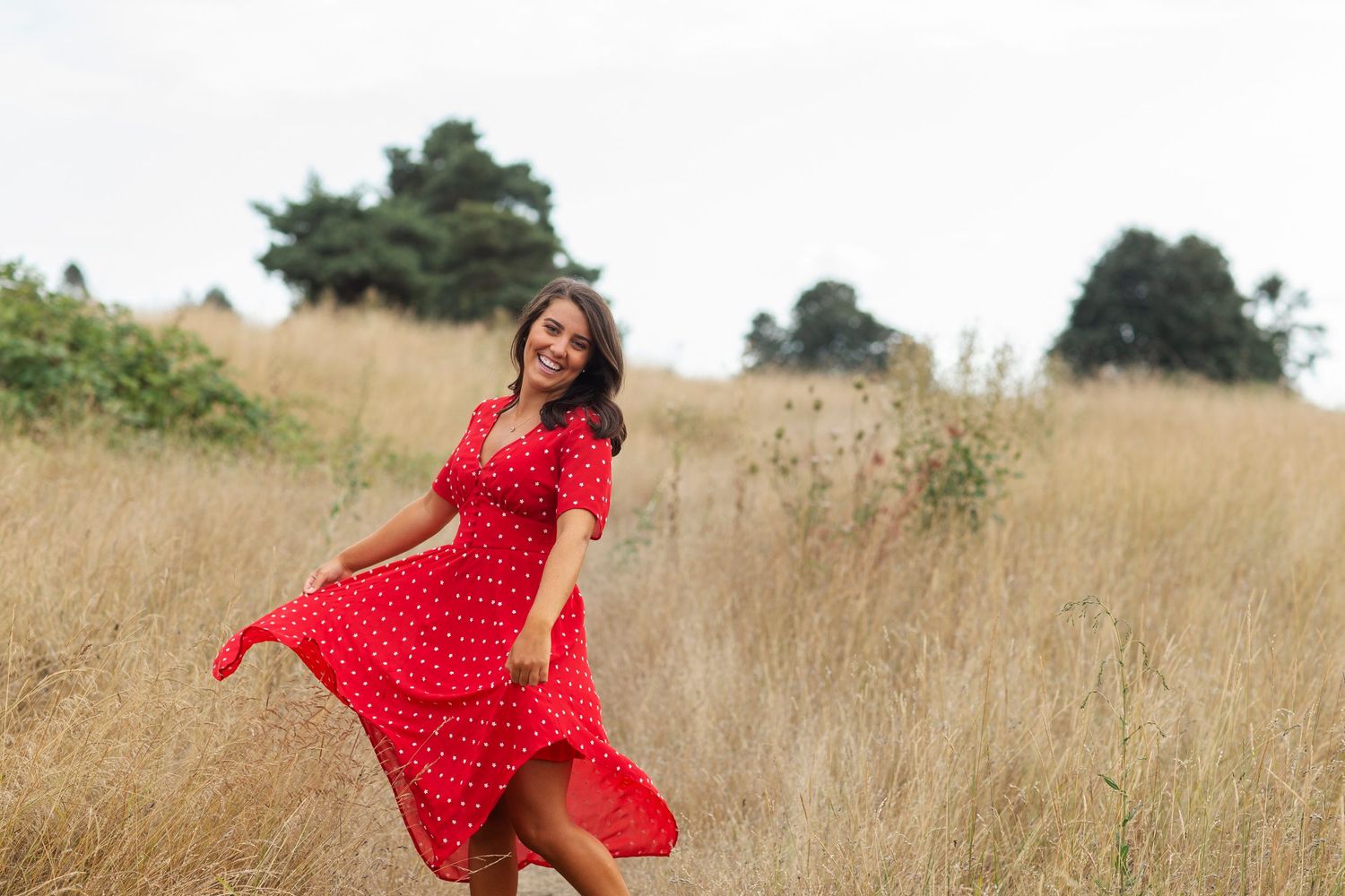 Young woman in red polka dot dress twirling in golden field.