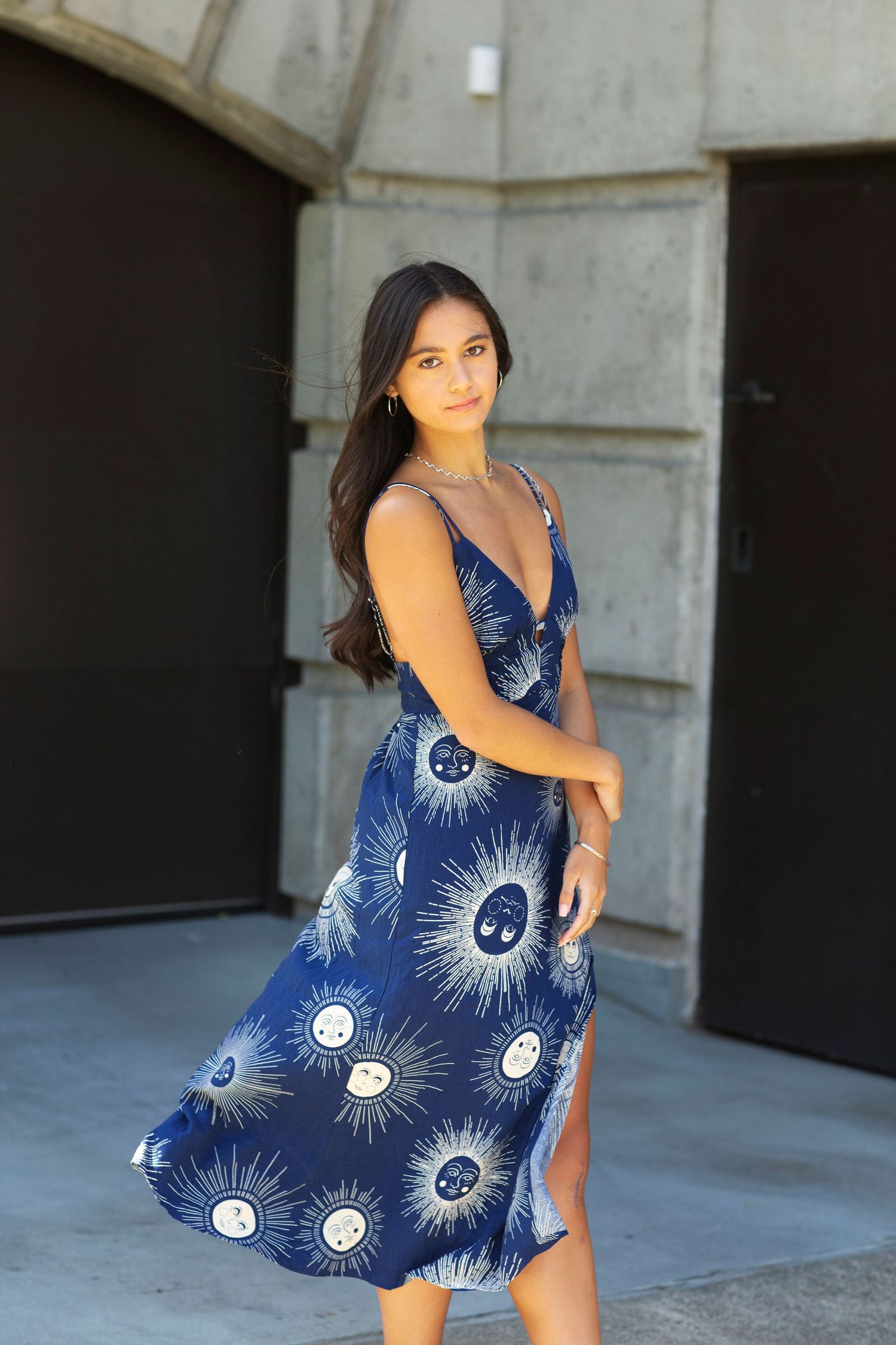 Young woman posing in a navy blue sun print midi dress with V-neckline in front of dark doors.