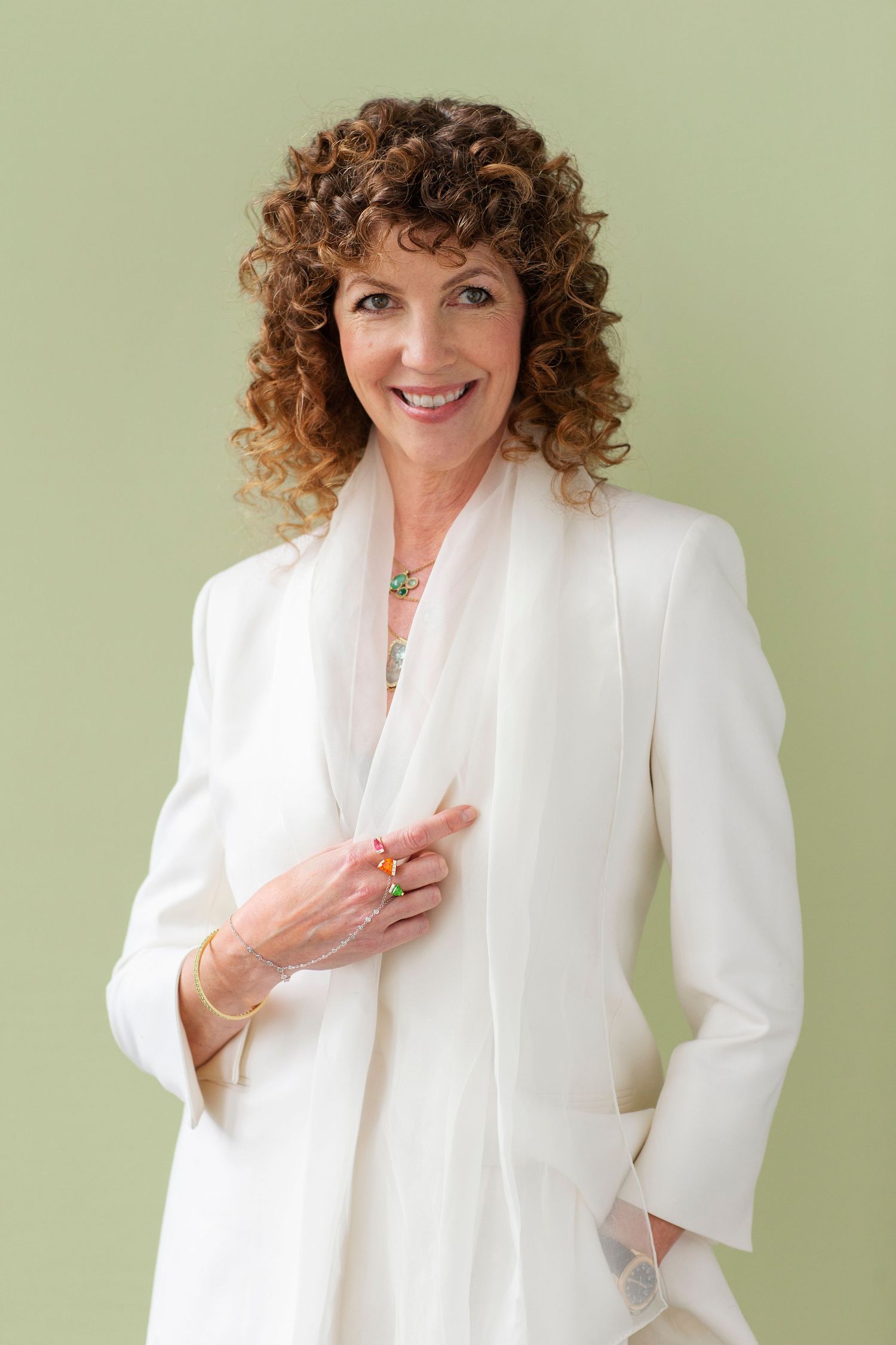 Older woman with curly hair in white blazer smiling on green background.