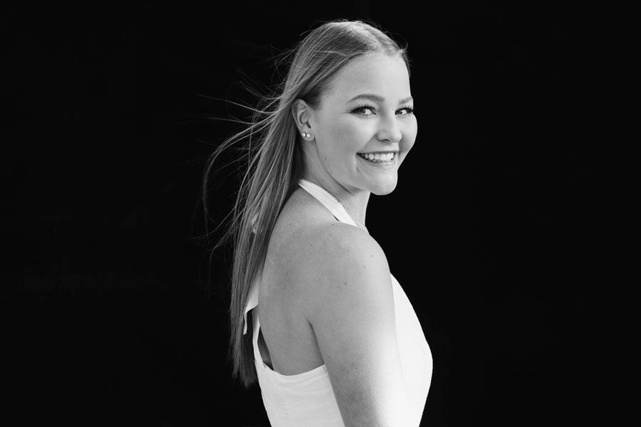 Black and white portrait of a smiling blonde woman in a white dress, looking over her shoulder elegantly.