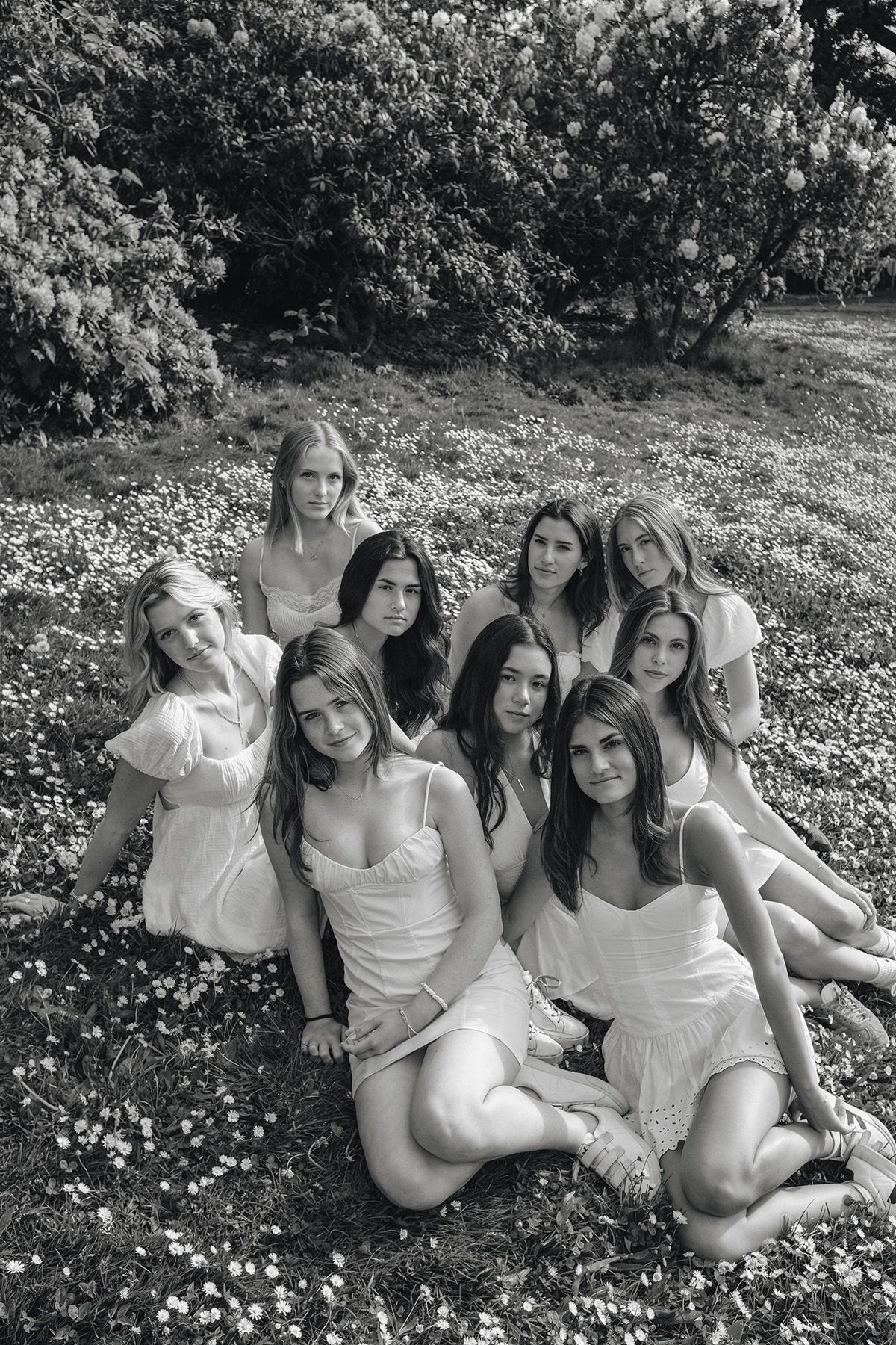 Black and white photo of a group of young women in white dresses posing together in a flower field.