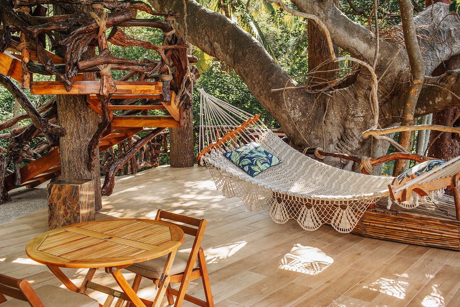 Relaxing hammock strung between trees on a sunny wooden deck with table and chairs in a tropical setting.