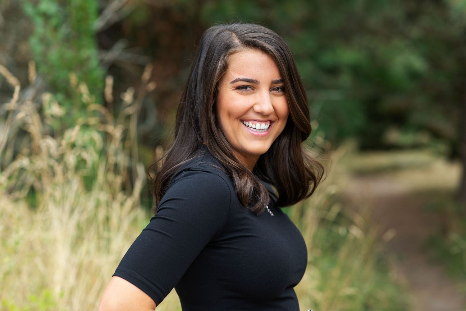 Happy brunette woman in black dress smiling on nature path.