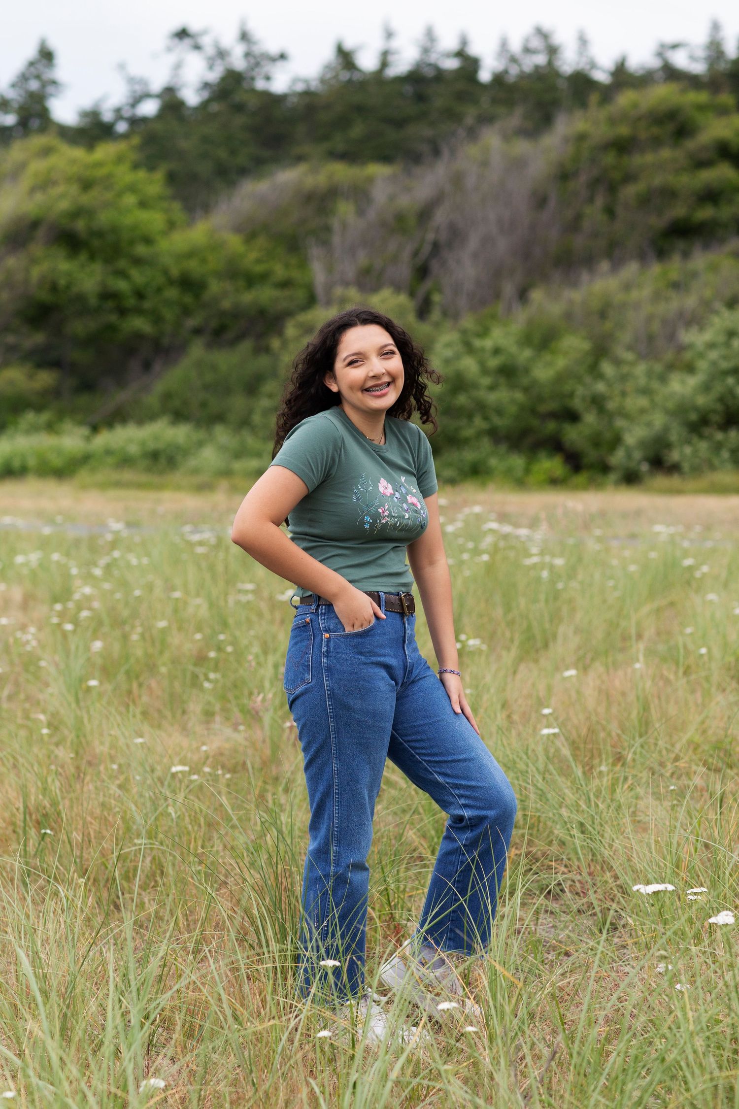 Happy young woman in green graphic tee and jeans posing in grassy meadow.
