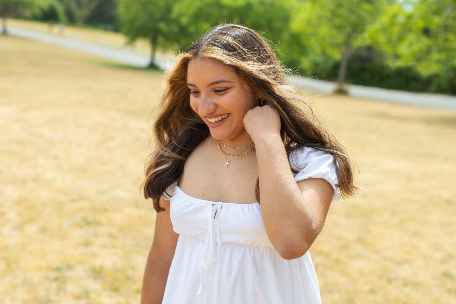 Young woman in white dress smiling outdoors in sunny park.
