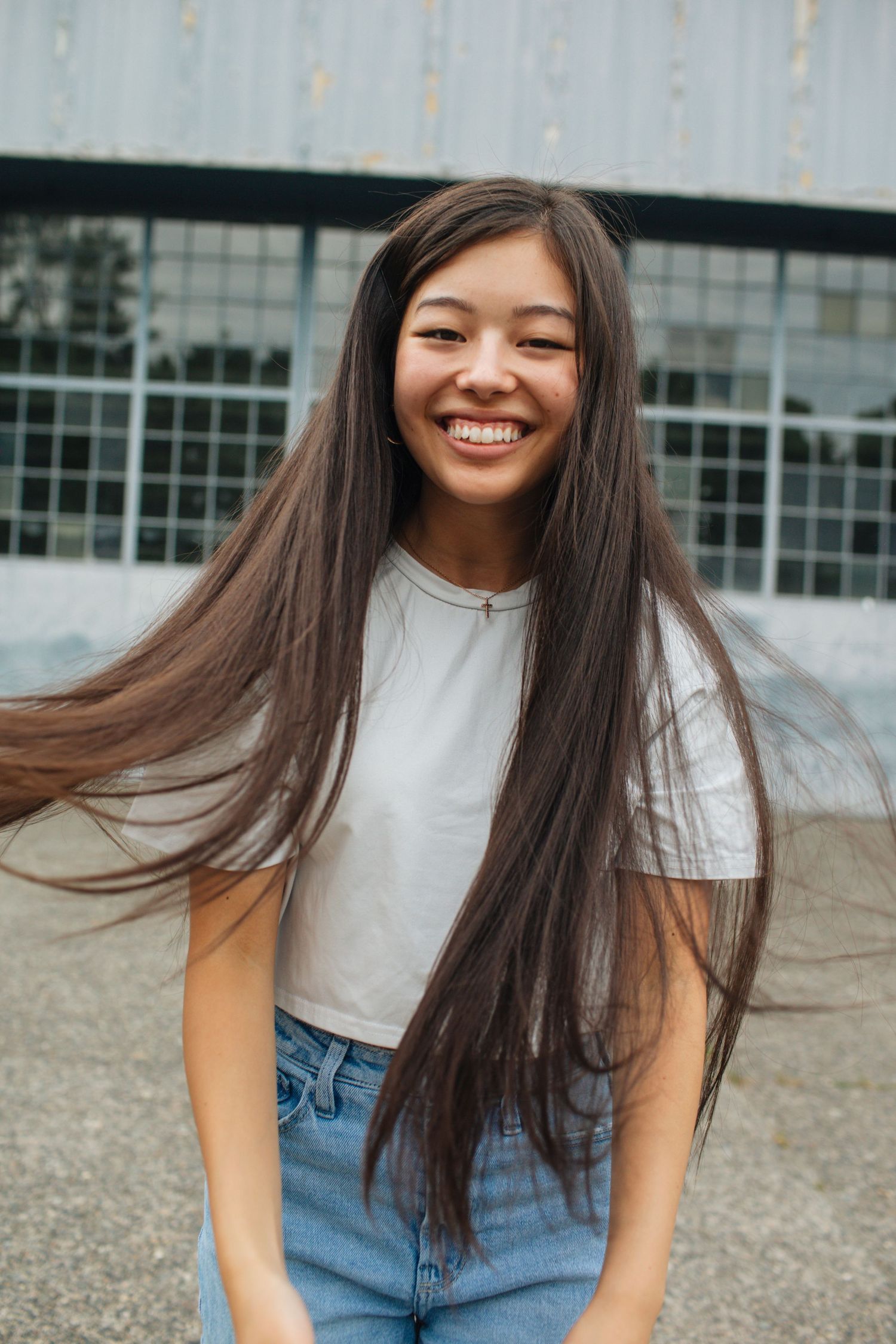 Young woman with long windswept hair laughing joyfully outdoors in white crop top and blue jeans.