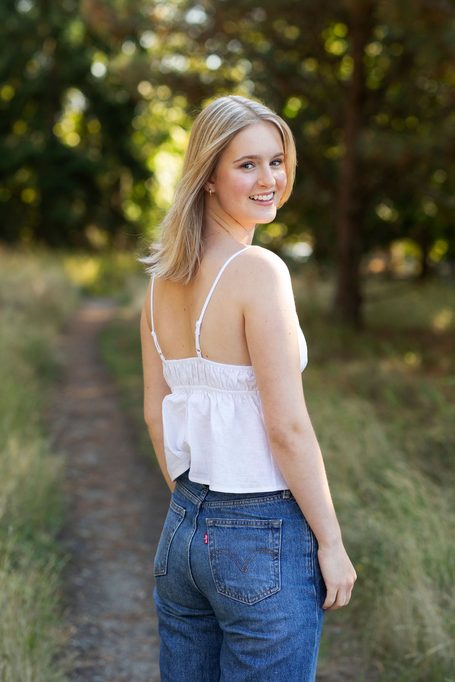 Blonde woman in white cami and Levis jeans looking back over shoulder on scenic dirt path.