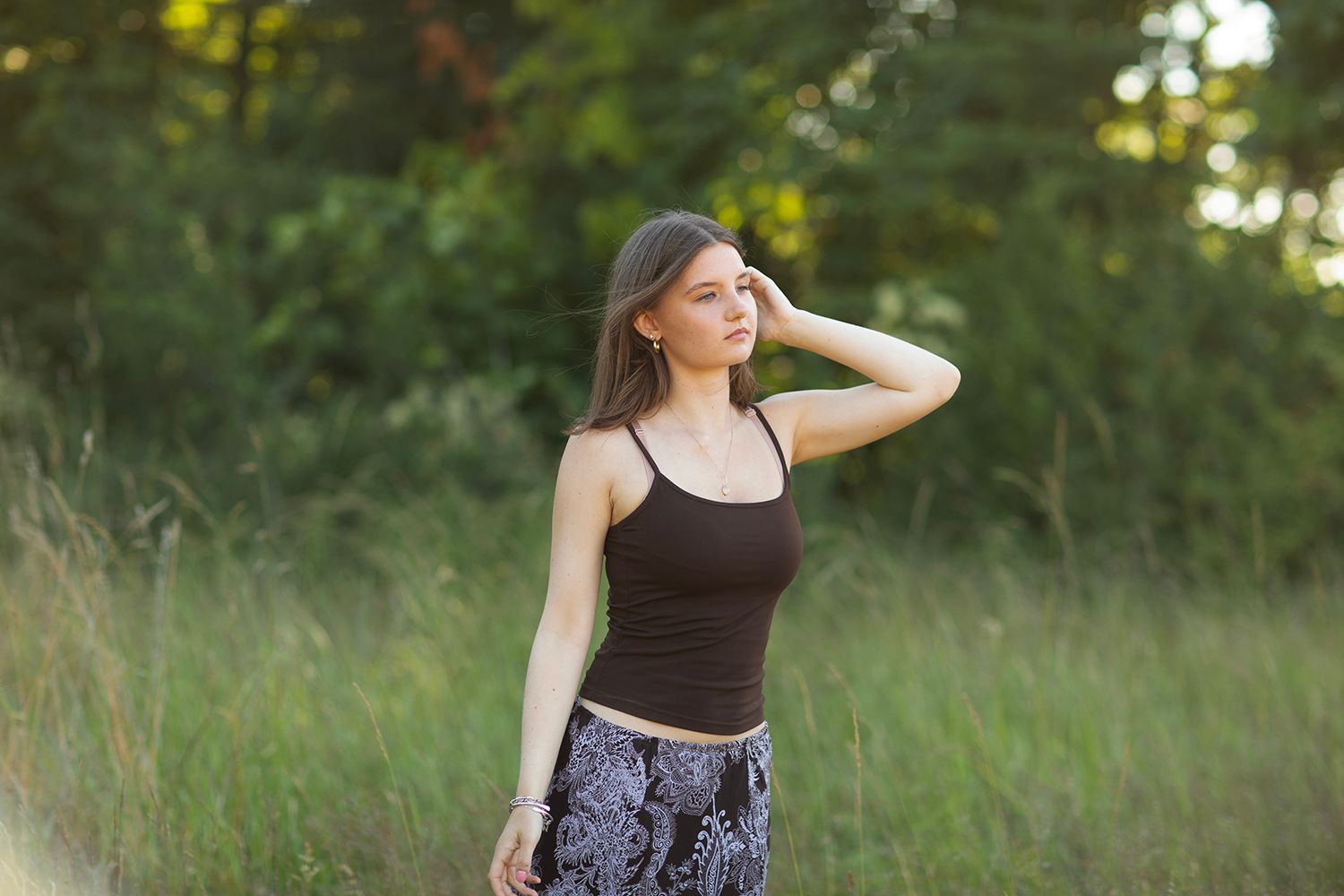 Young woman in black crop top and patterned skirt posing in lush green field outdoors.