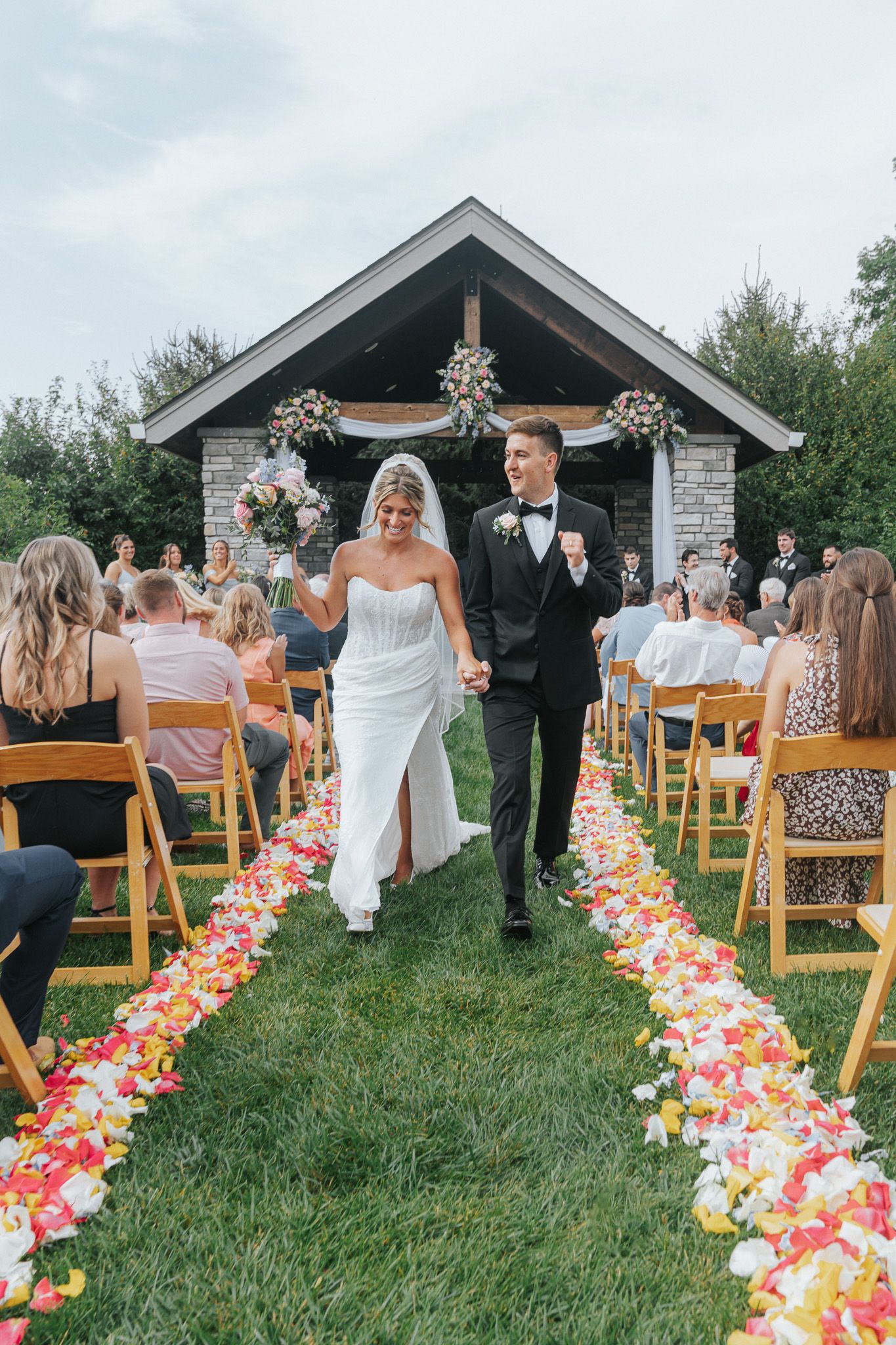 Newlyweds holding hands walking down colorful rose petal aisle after ceremony.