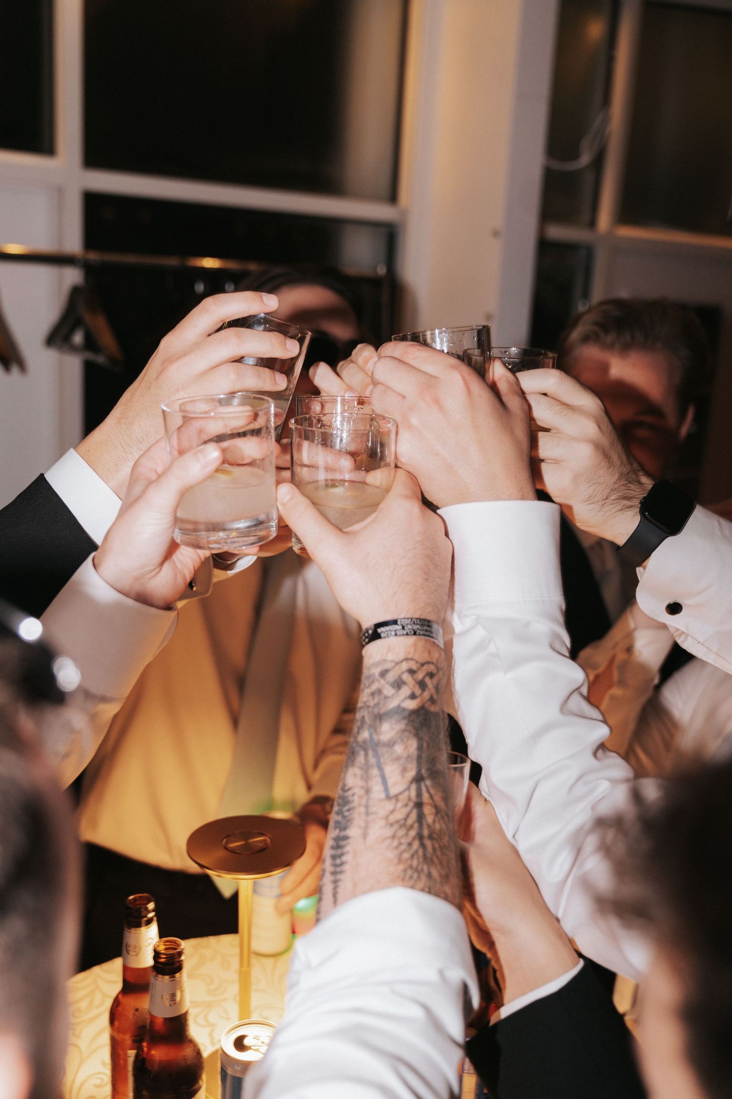 Group of men in formal wear clinking shot glasses together in a celebratory toast at a bar event.