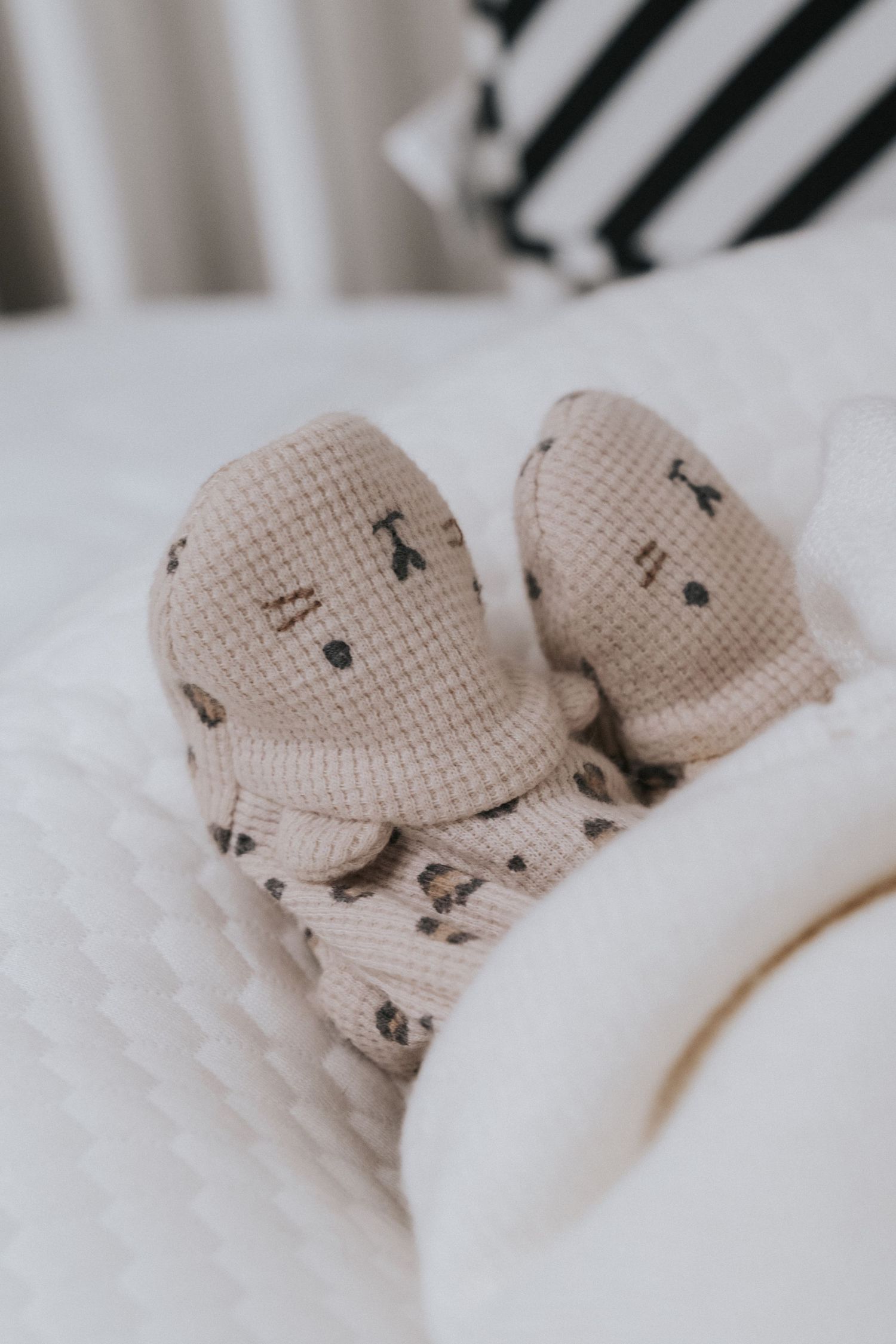 Close-up of adorable newborn baby feet in beige knit mittens on a white quilted blanket.