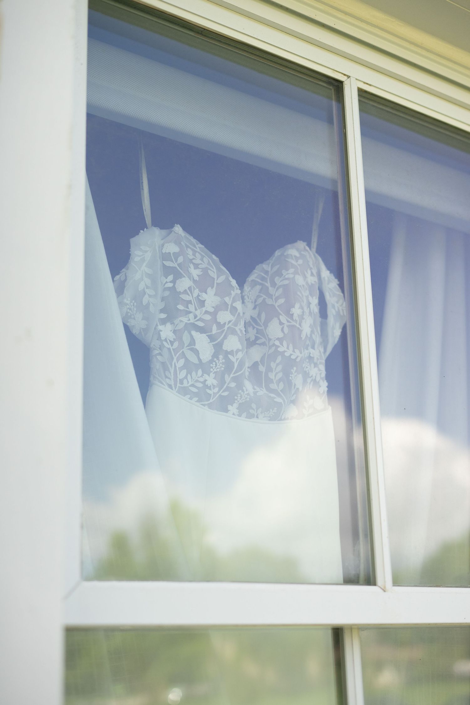Elegant white lace bridal gown bodice displayed in a bright window frame.