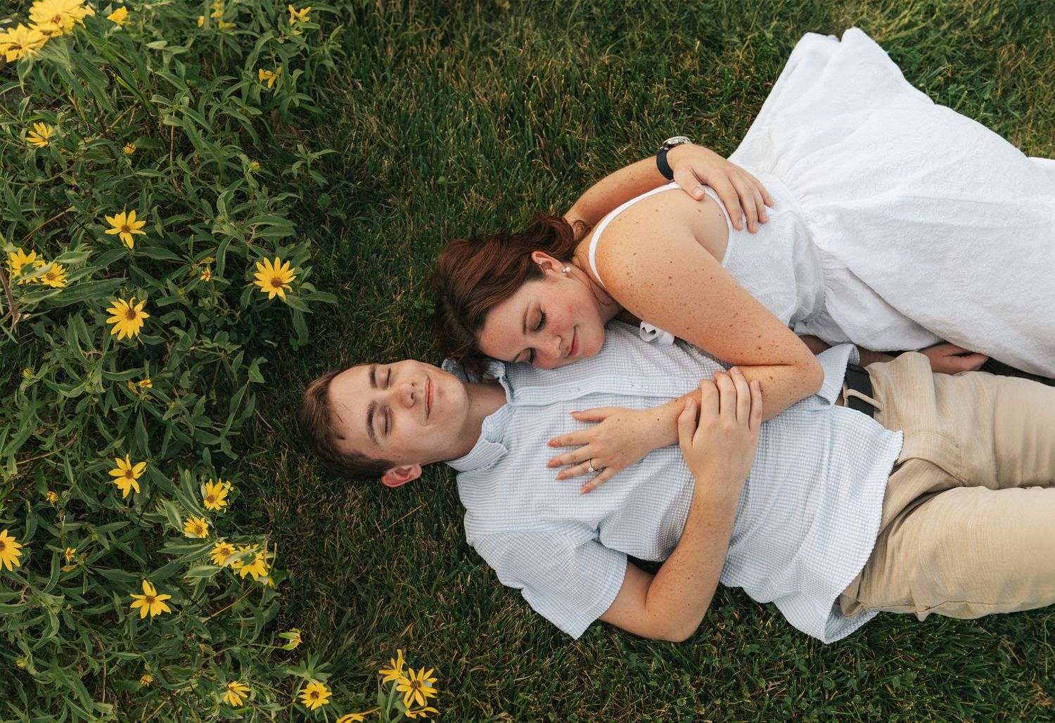 A romantic couple lies together in a field of yellow wildflowers, woman embracing man peacefully.