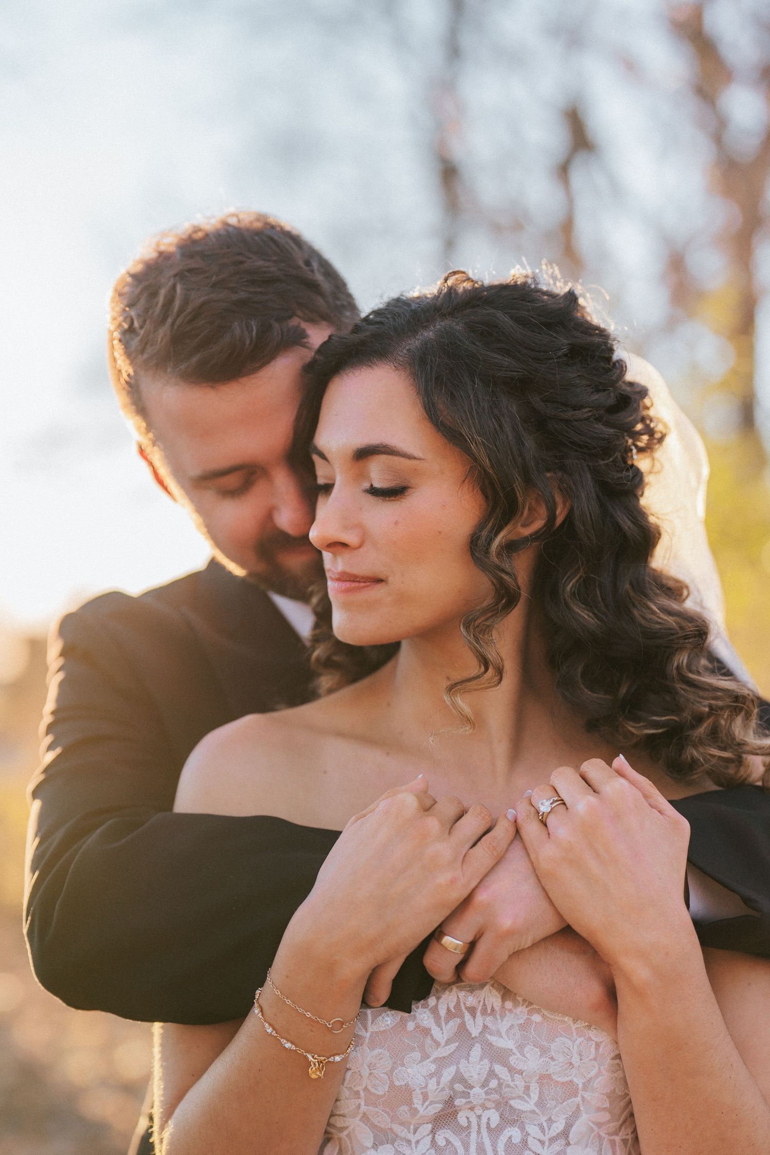 Romantic wedding portrait in warm sunset light with bride in lace dress and groom in dark suit.