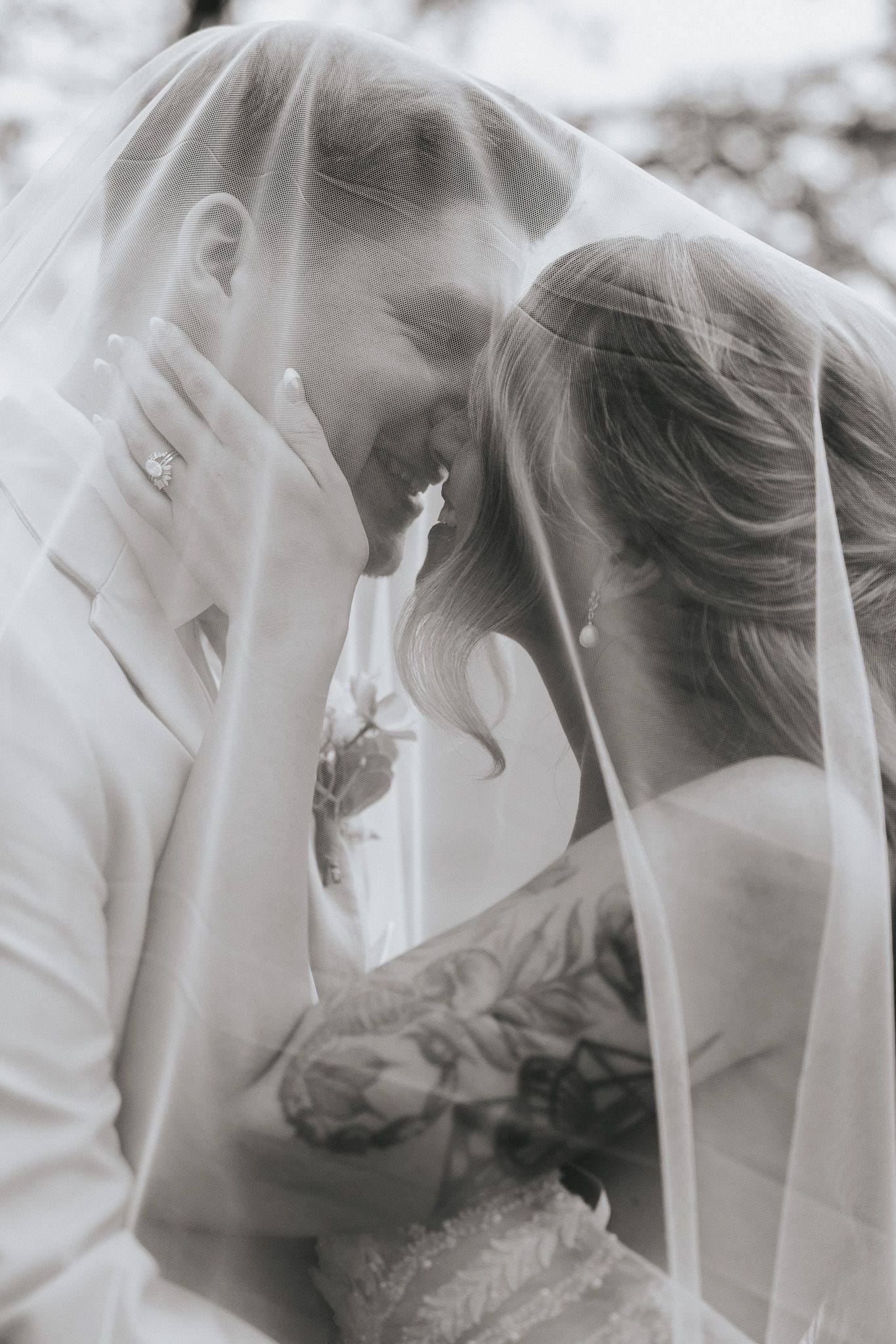 Black and white wedding photo of bride and groom sharing an intimate moment under a flowing veil.