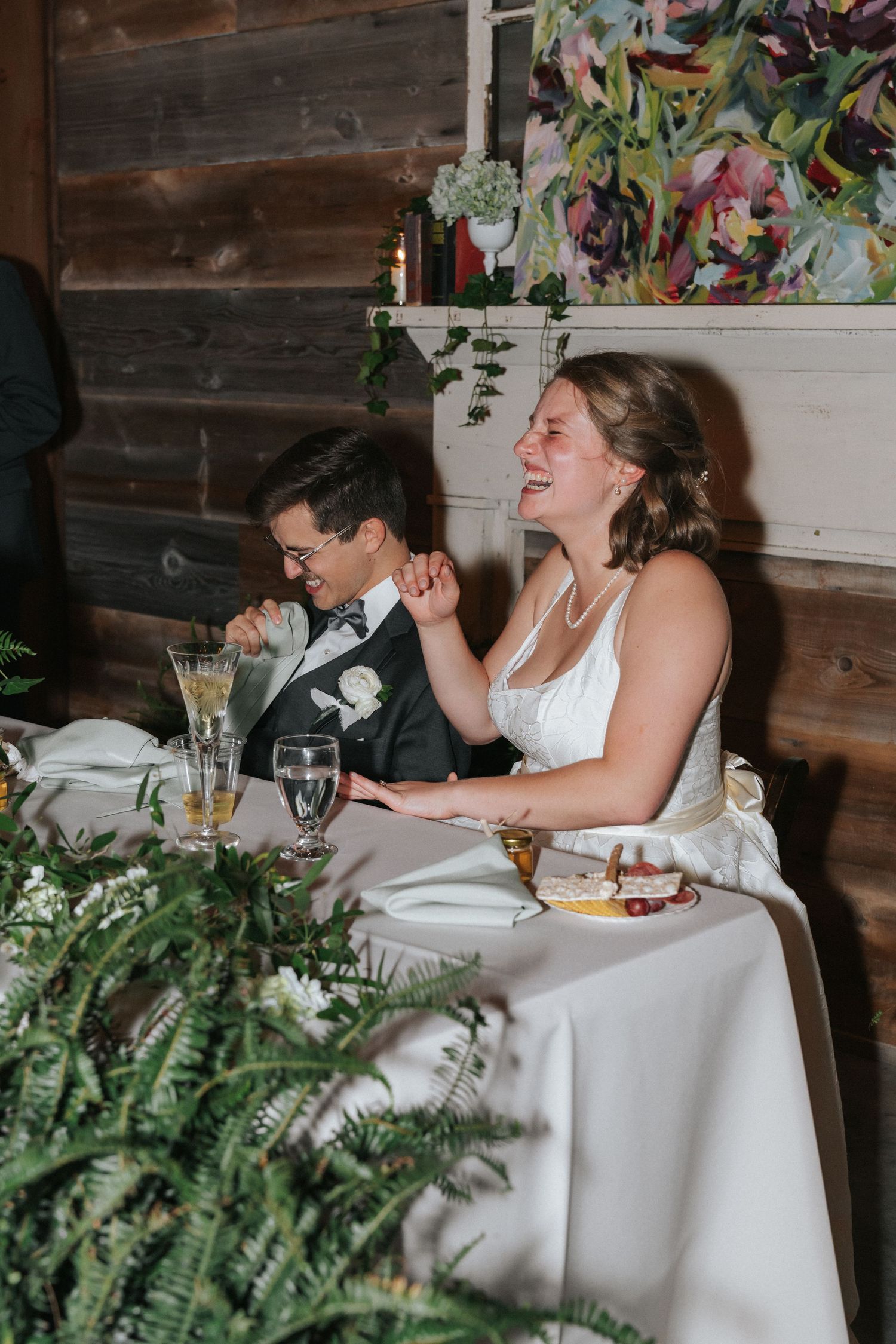 Bride and groom laughing together at sweetheart table during rustic barn wedding reception.