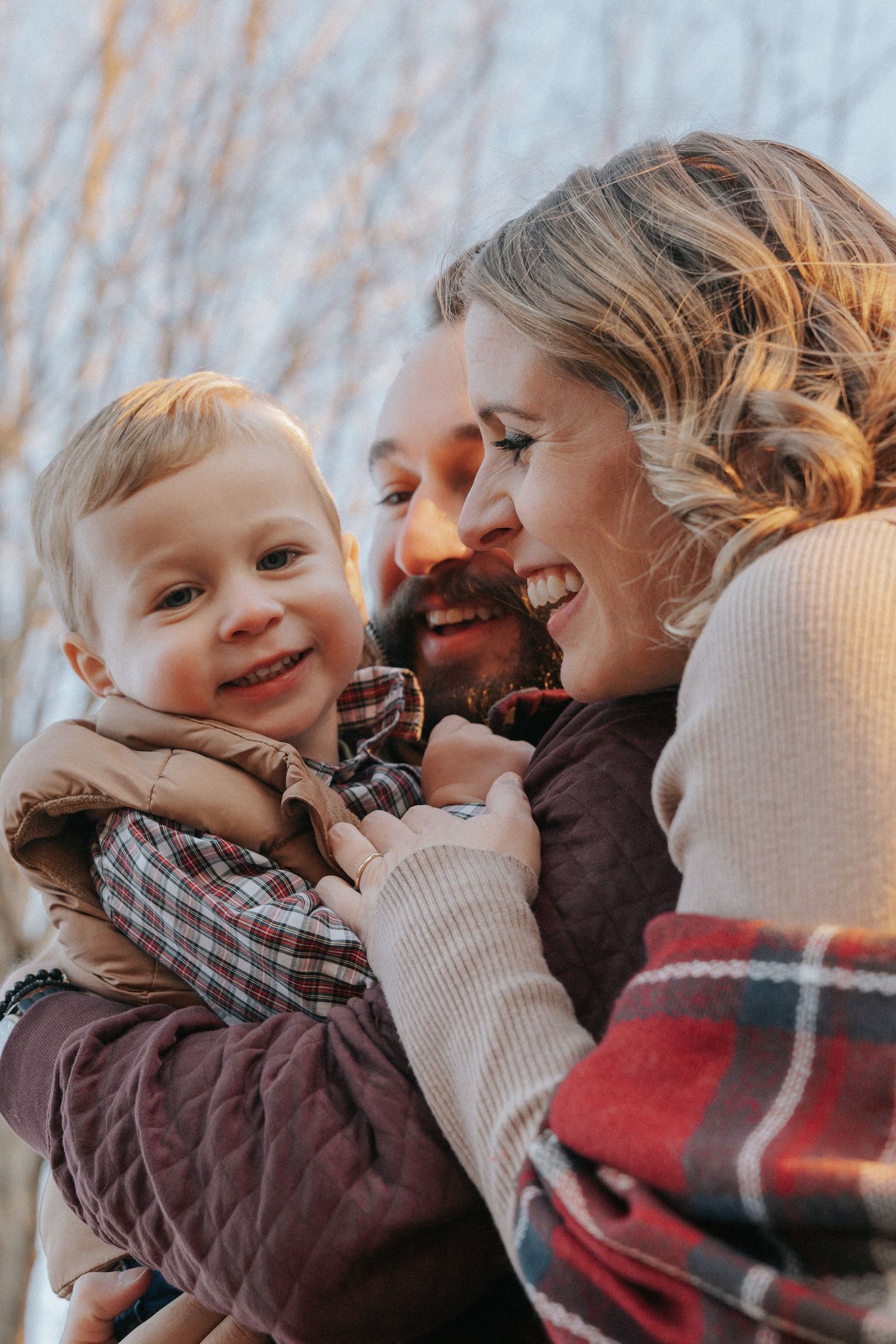 Joyful family portrait with smiling toddler held by laughing parents in warm sunset light.