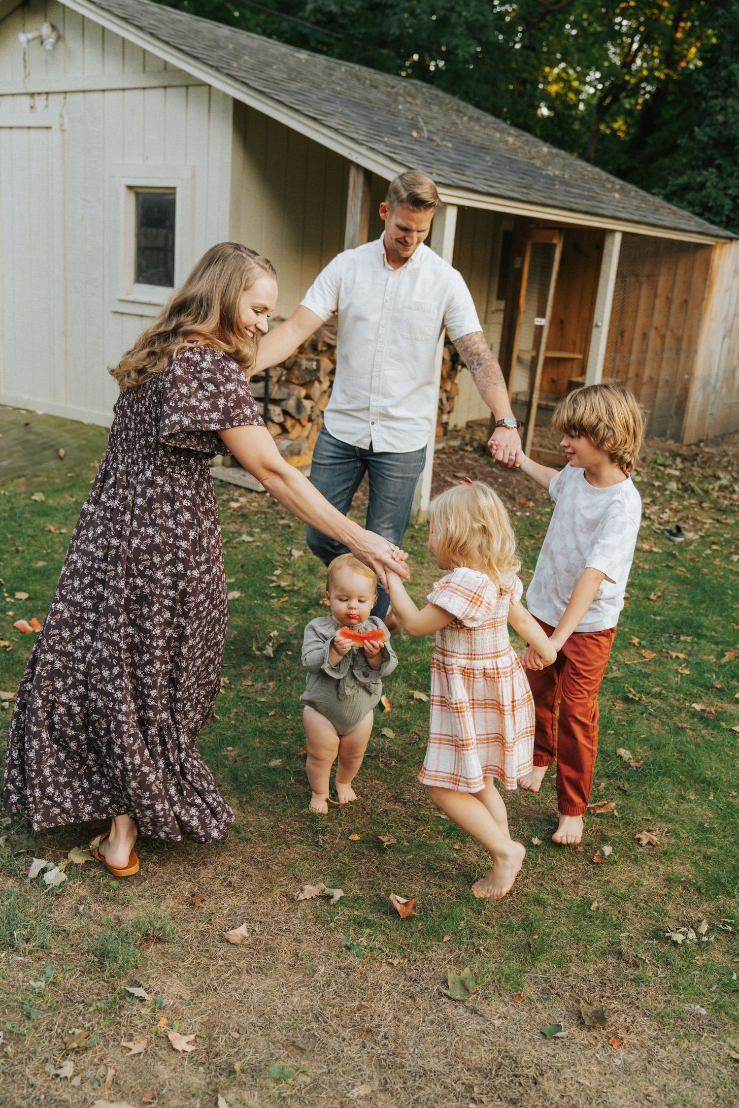 Happy family of five holding hands and dancing together in backyard near rustic barn in autumn.