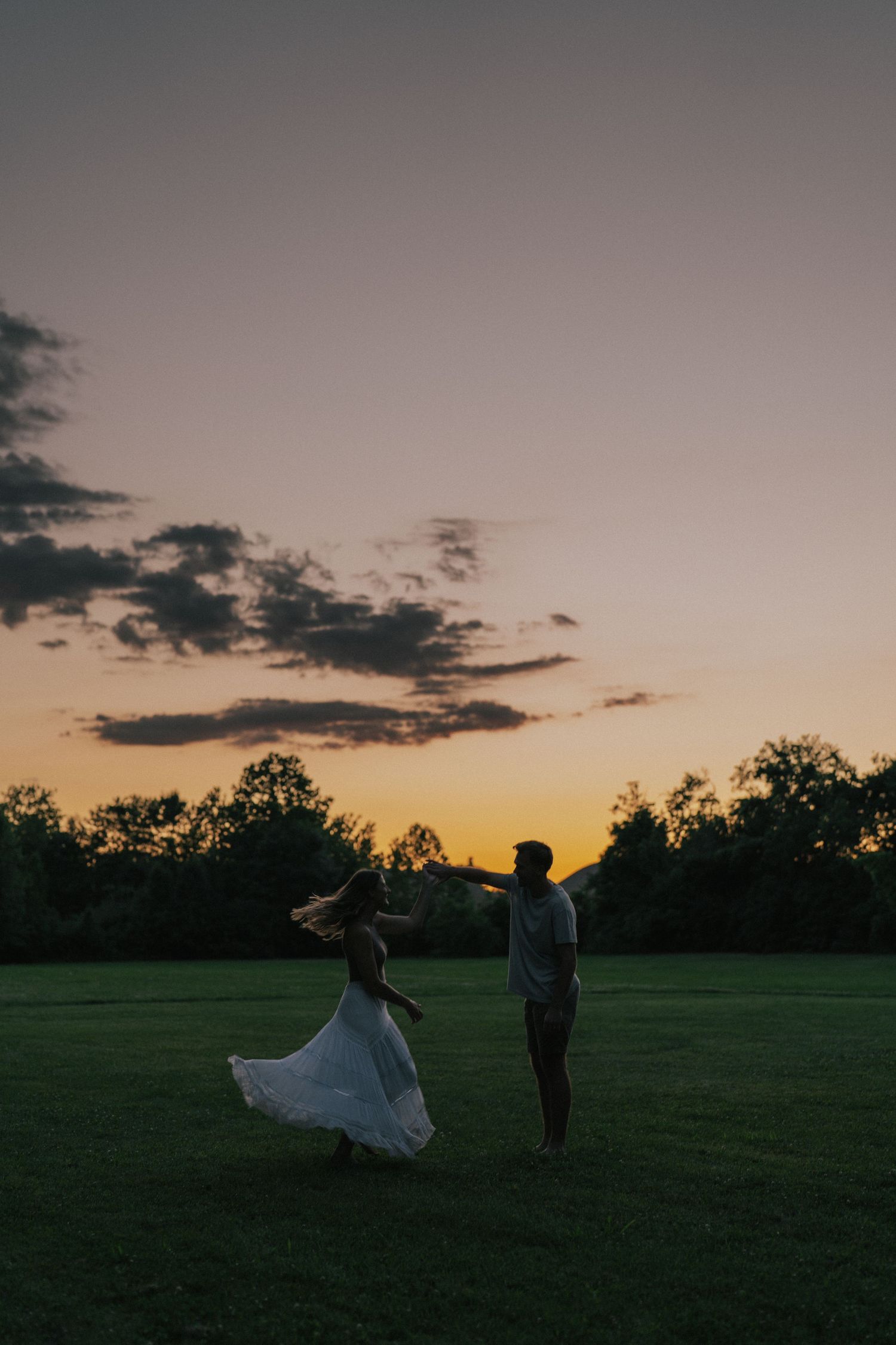Silhouette of couple dancing in a field during a golden sunset with trees in the background.