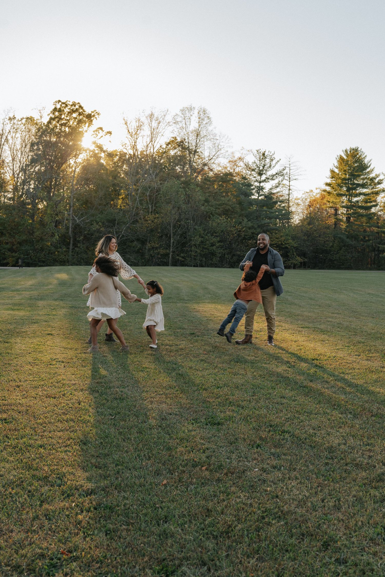 Happy family playing together in a sunny green field at golden hour with trees in the background.