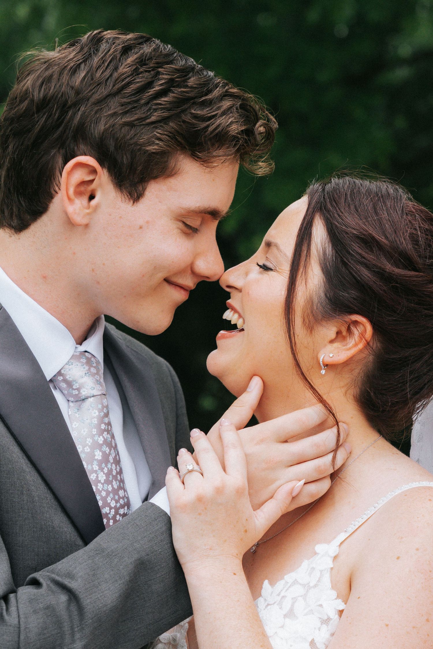 A joyful bride and groom share an intimate moment, nearly kissing, with the bride laughing and wearing a white lace gown.