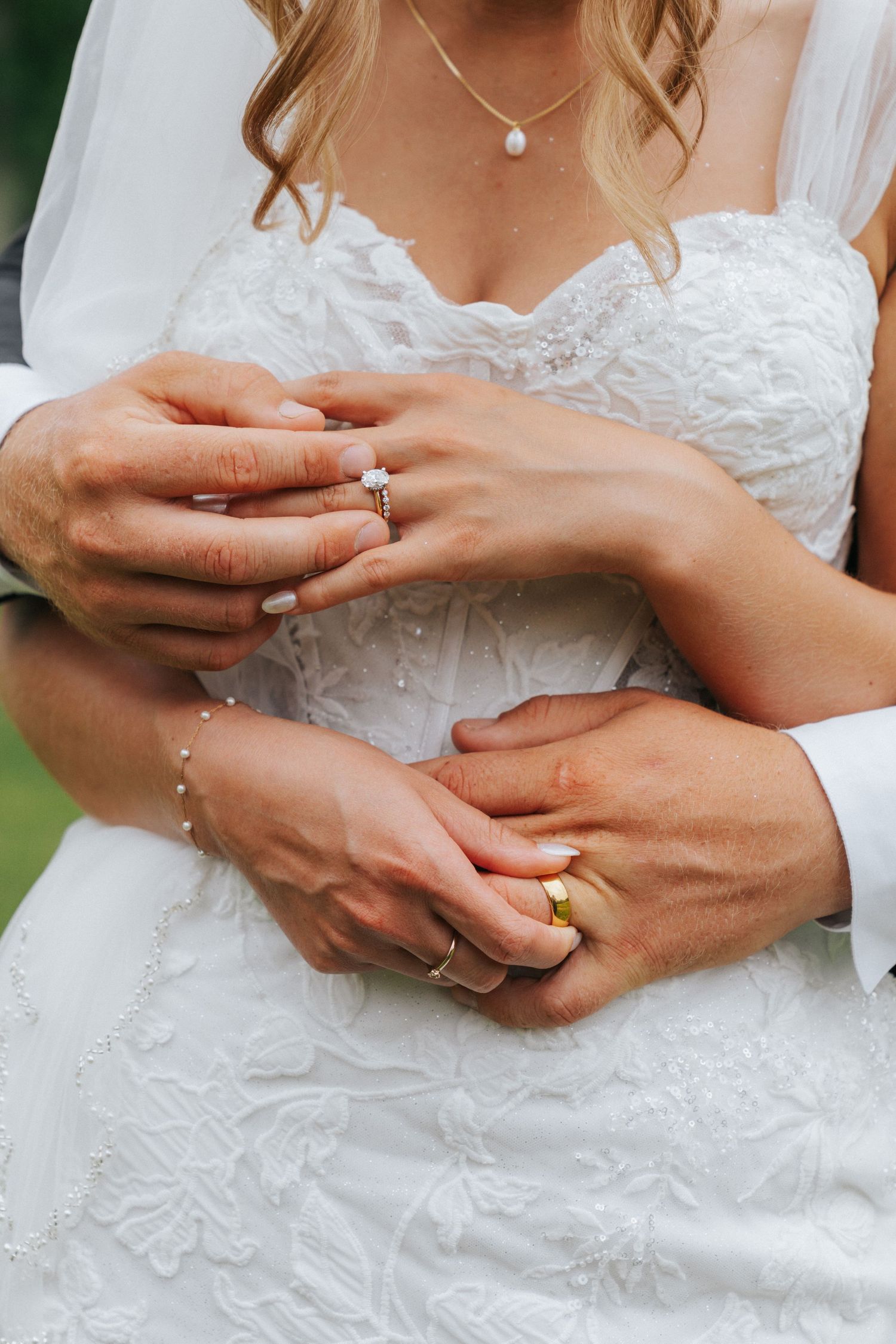 Bride and groom showing wedding rings, hands intertwined over white lace bridal gown.