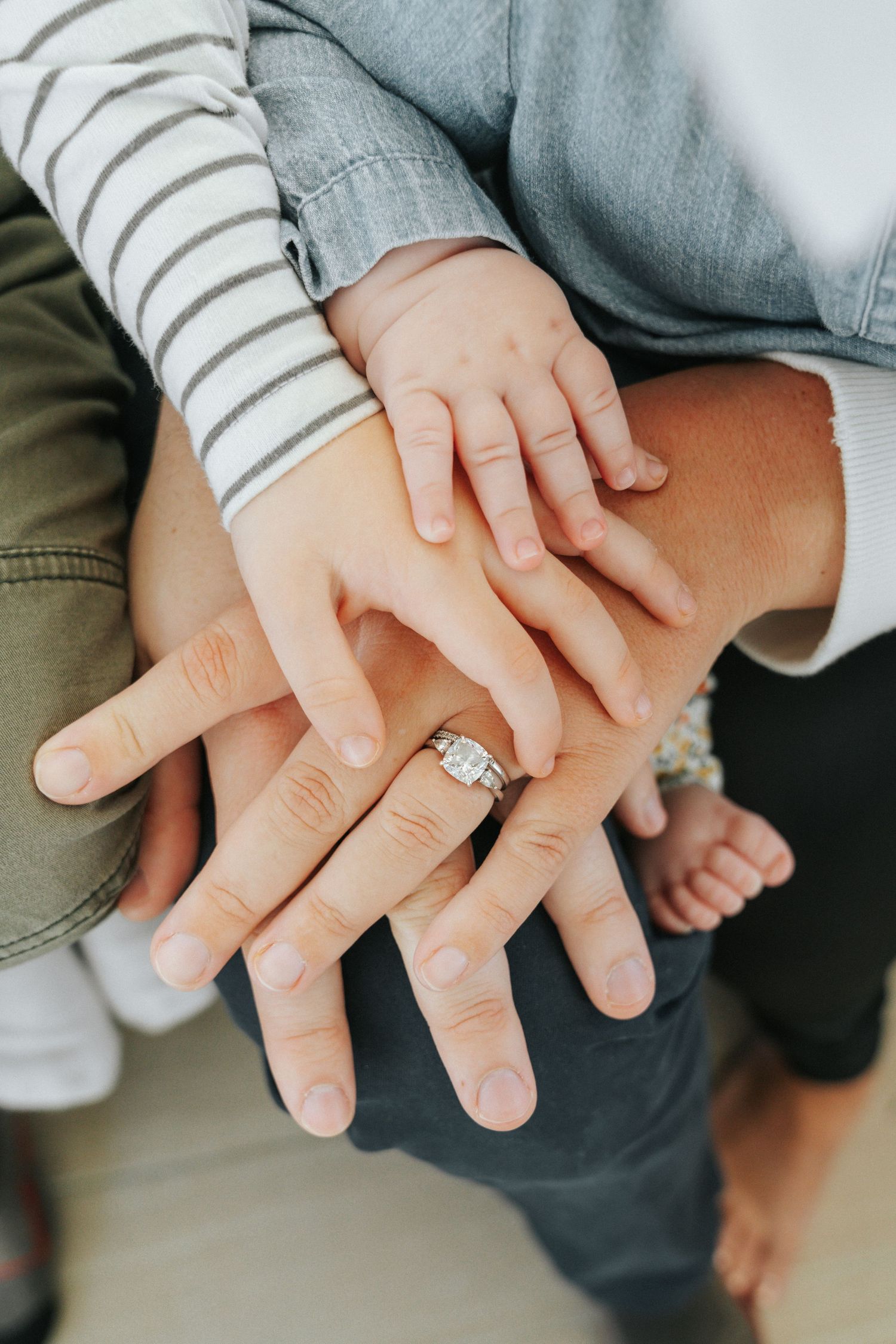 A family stacks their hands together showing a diamond engagement ring, including a baby's tiny hand.