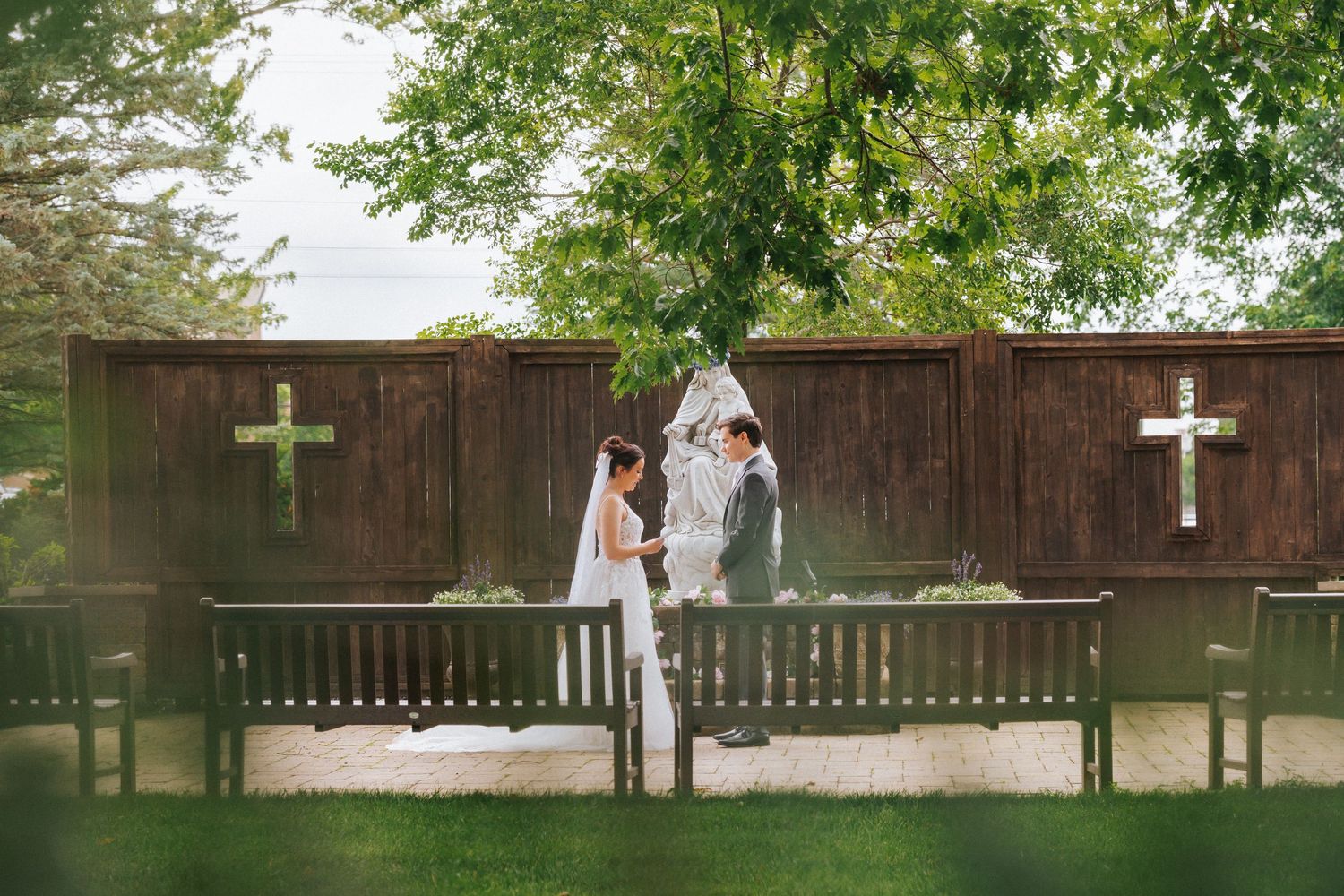 Couple exchanging vows outdoors at a rustic wedding ceremony with wooden fence and crosses backdrop.