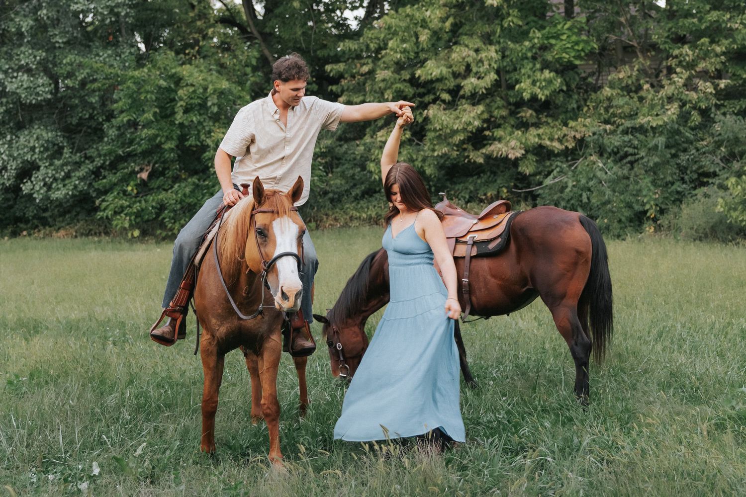 A couple with two brown horses in a green field, the man on horseback holding the womans hand.