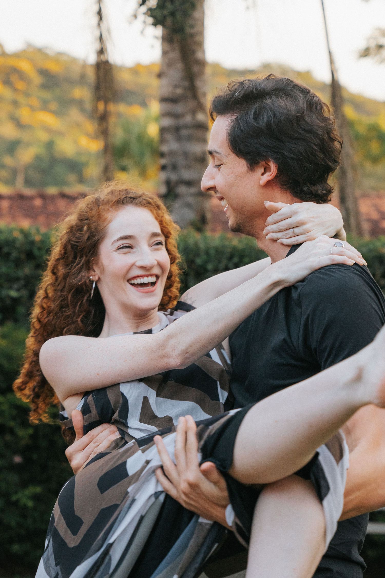 Man carrying laughing redhead woman in his arms during a romantic outdoor couples portrait session.