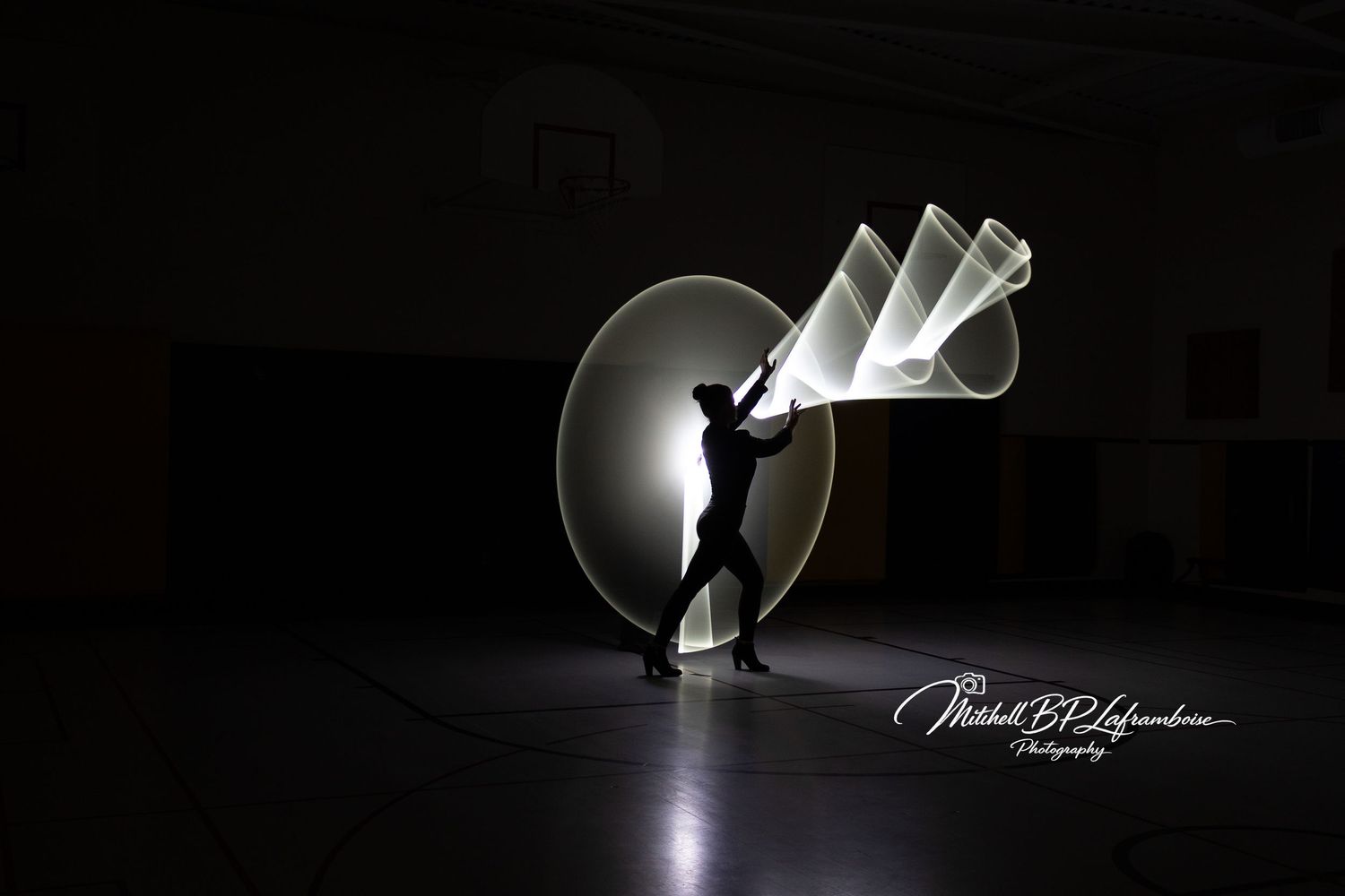 Person silhouette with white spiral and cone light painting shapes in a dark gymnasium.