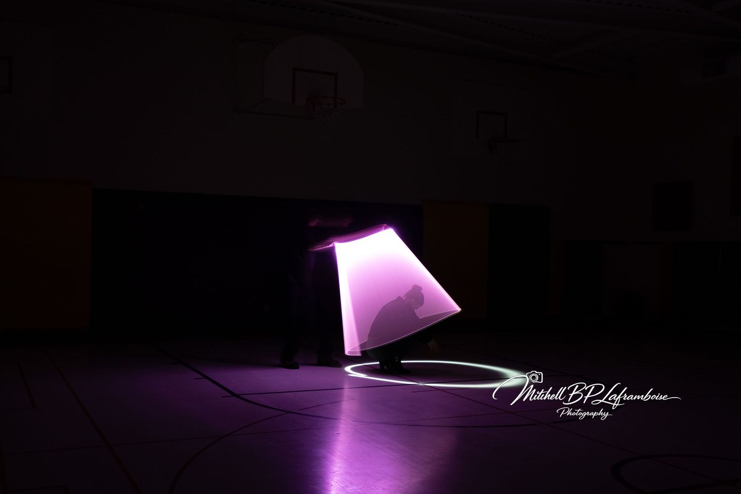 Purple glowing geometric lamp shape created with light painting photography in a dark gym.