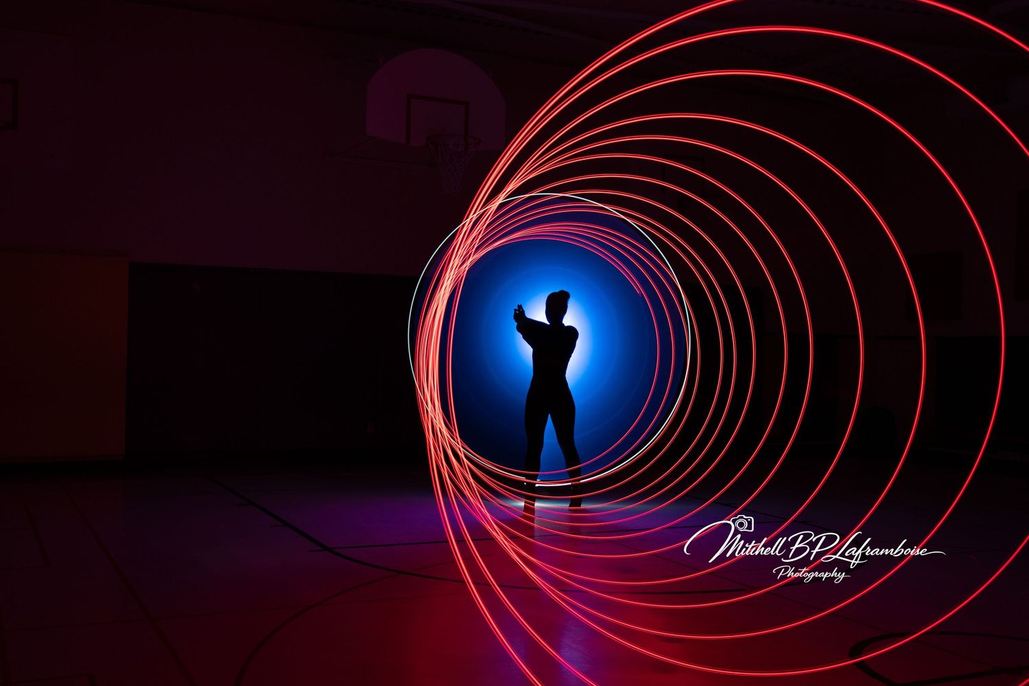 Silhouette of a person surrounded by glowing red spiral light painting in a dark gymnasium.