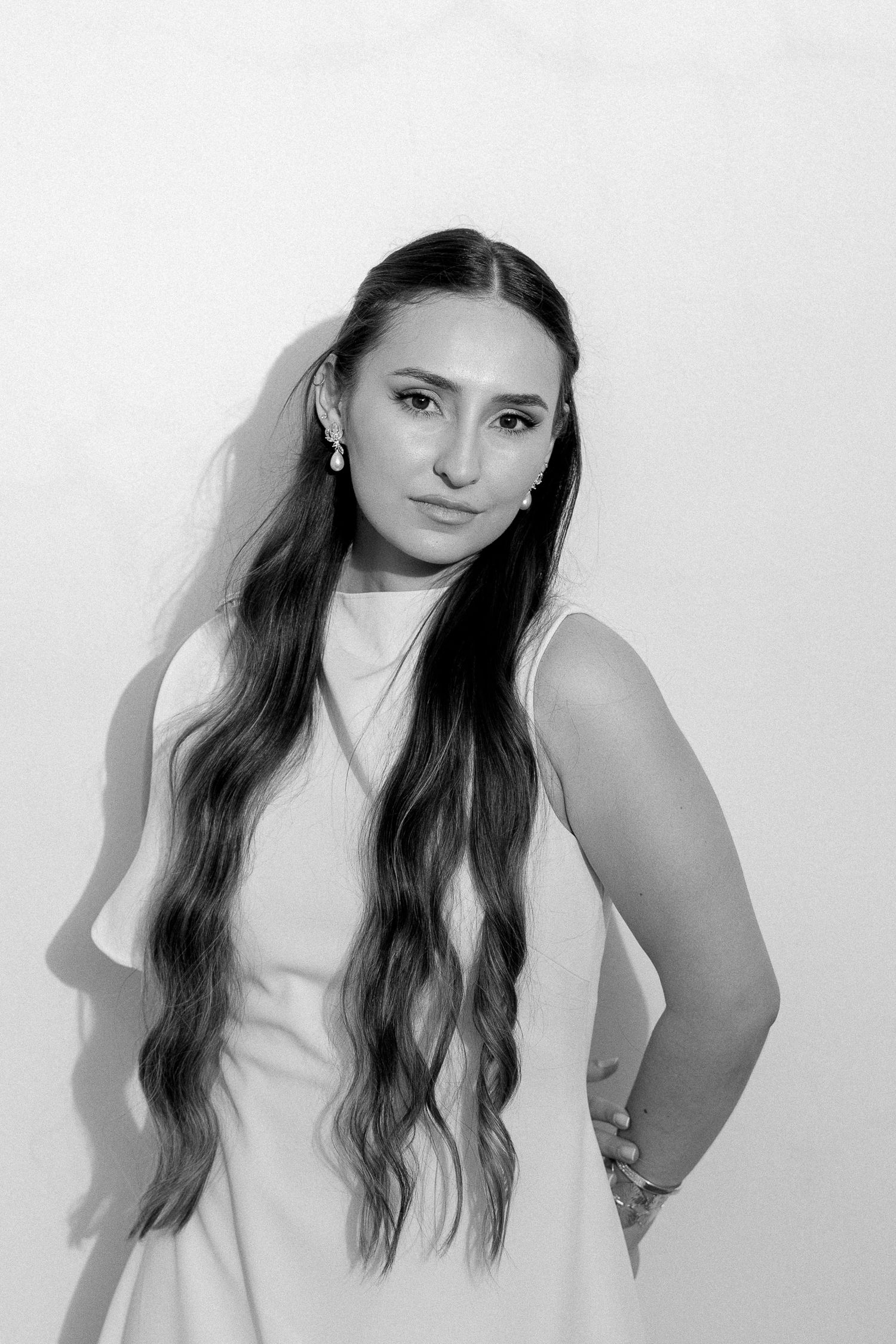 Black and white portrait of a young woman with long wavy hair wearing a sleeveless dress, posing confidently.