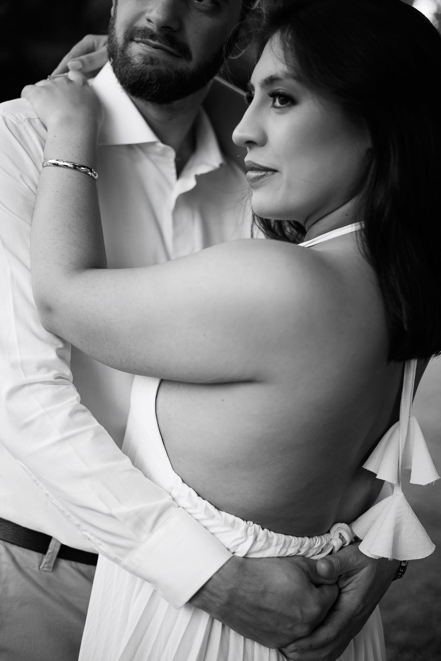 Black and white photo of a couple embracing, woman in backless white dress, man in white shirt holding her close.