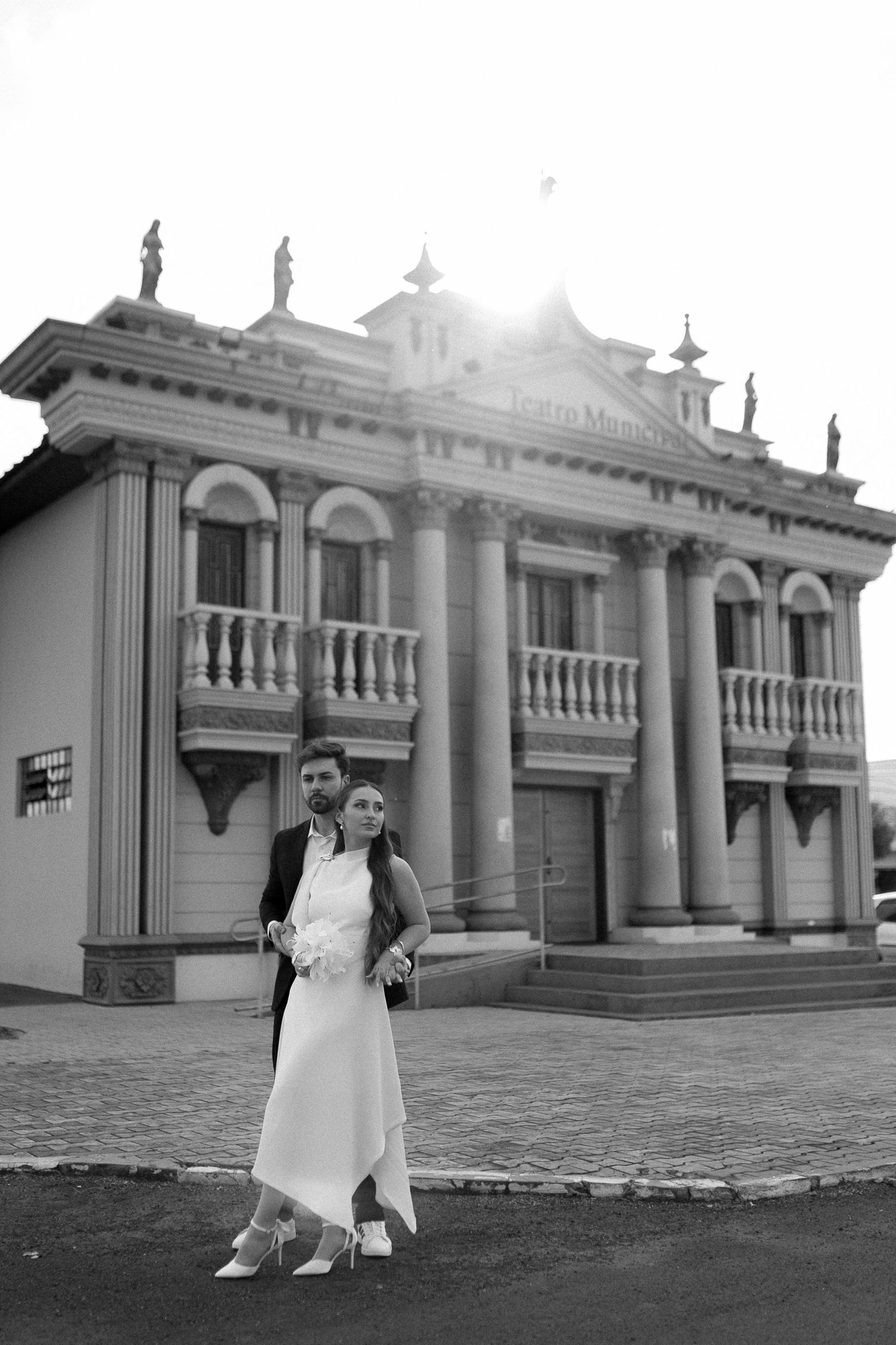 Black and white wedding photo of bride and groom embracing in front of a grand neoclassical building.