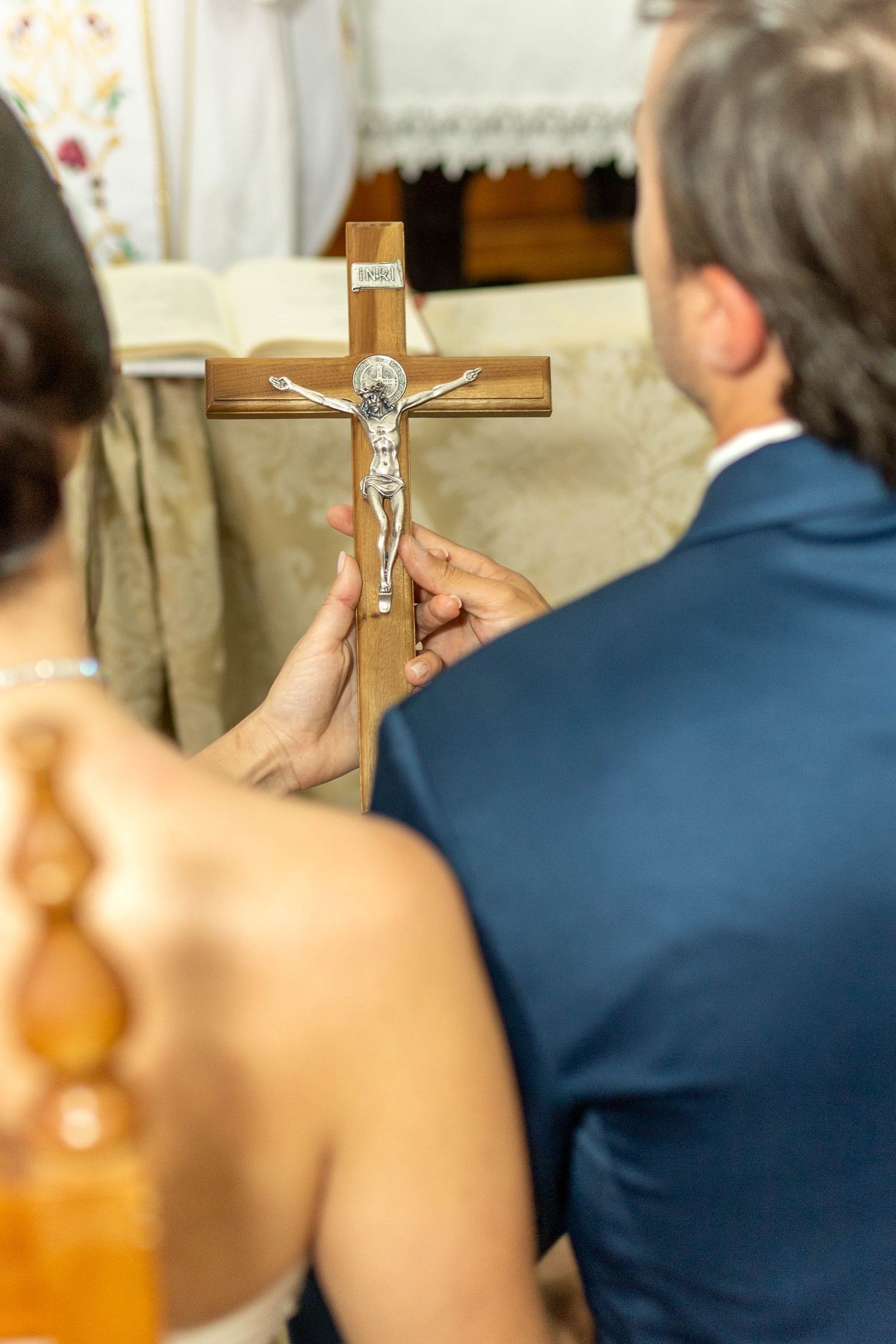 Couple holding a wooden crucifix with silver Jesus figure during a Catholic wedding ceremony in church.