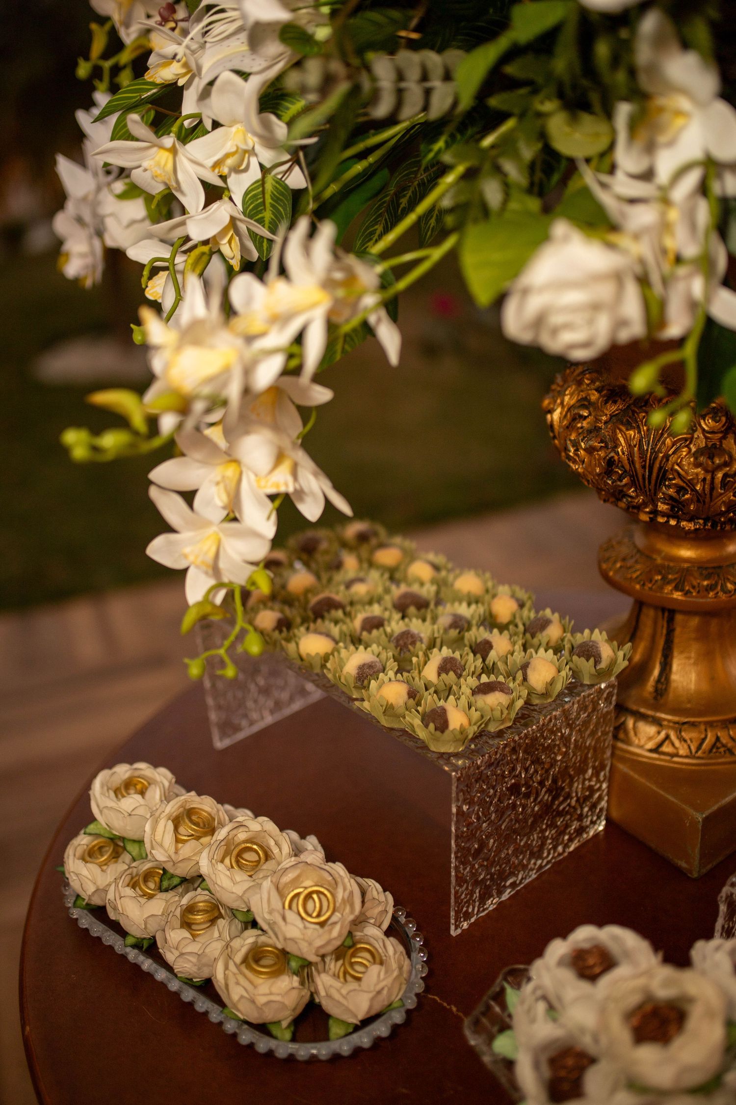 Elegant wedding dessert table with rose-shaped pastries, chocolate truffles, white orchids, and a gold decorative vase.