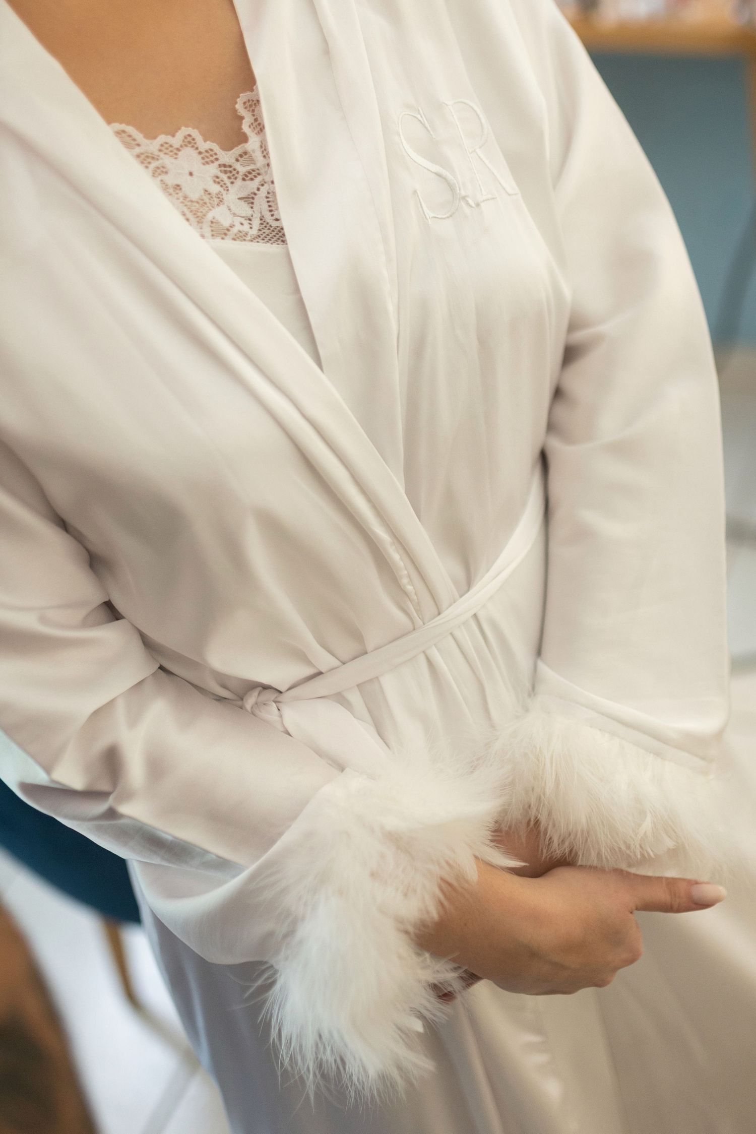 Woman wearing a white satin bridal robe with feather cuffs and lace details, tied at the waist.