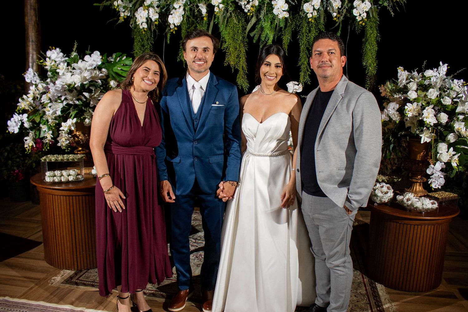 Bride and groom pose with family members at elegant floral wedding reception backdrop with white flowers.