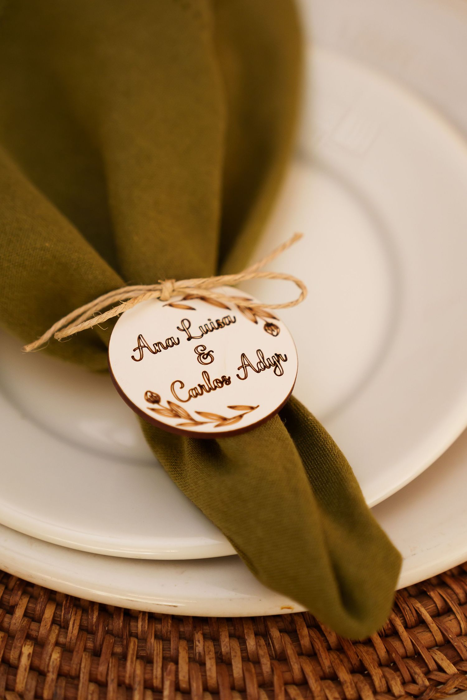 Elegant wedding place setting with olive green napkin, white plates, and wooden tag engraved with Ana Luisa & Carlos Adyr.