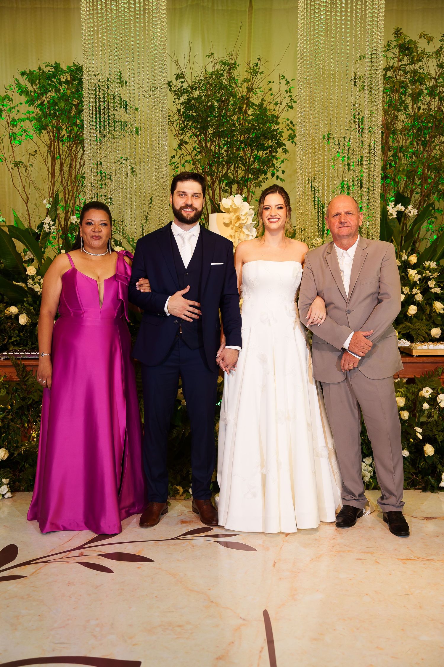 Wedding party poses with bride in white gown, groom in navy suit, woman in magenta dress, and man in gray suit.