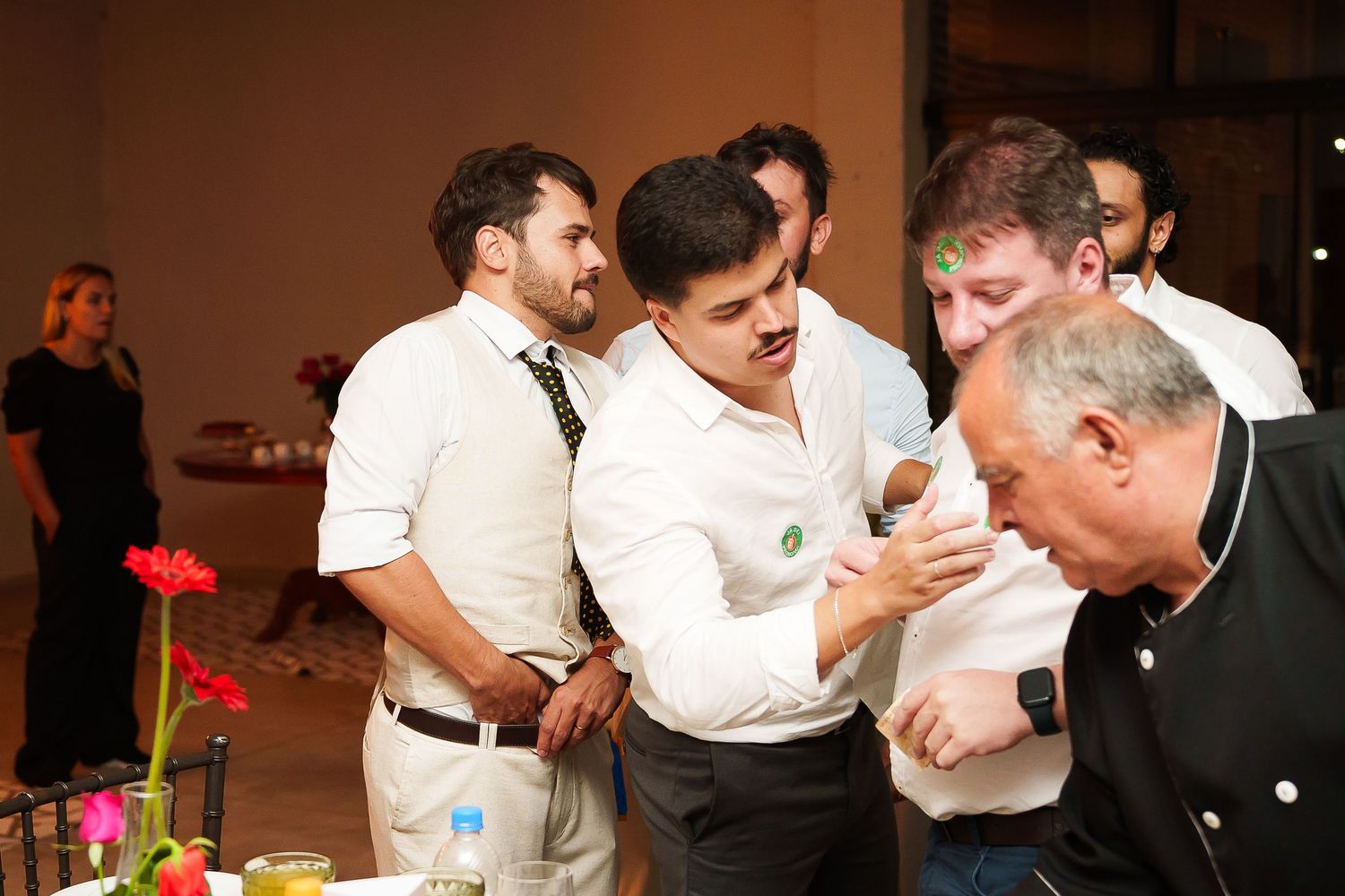 Group of men in formal attire engaged in conversation at an indoor event with floral decorations.