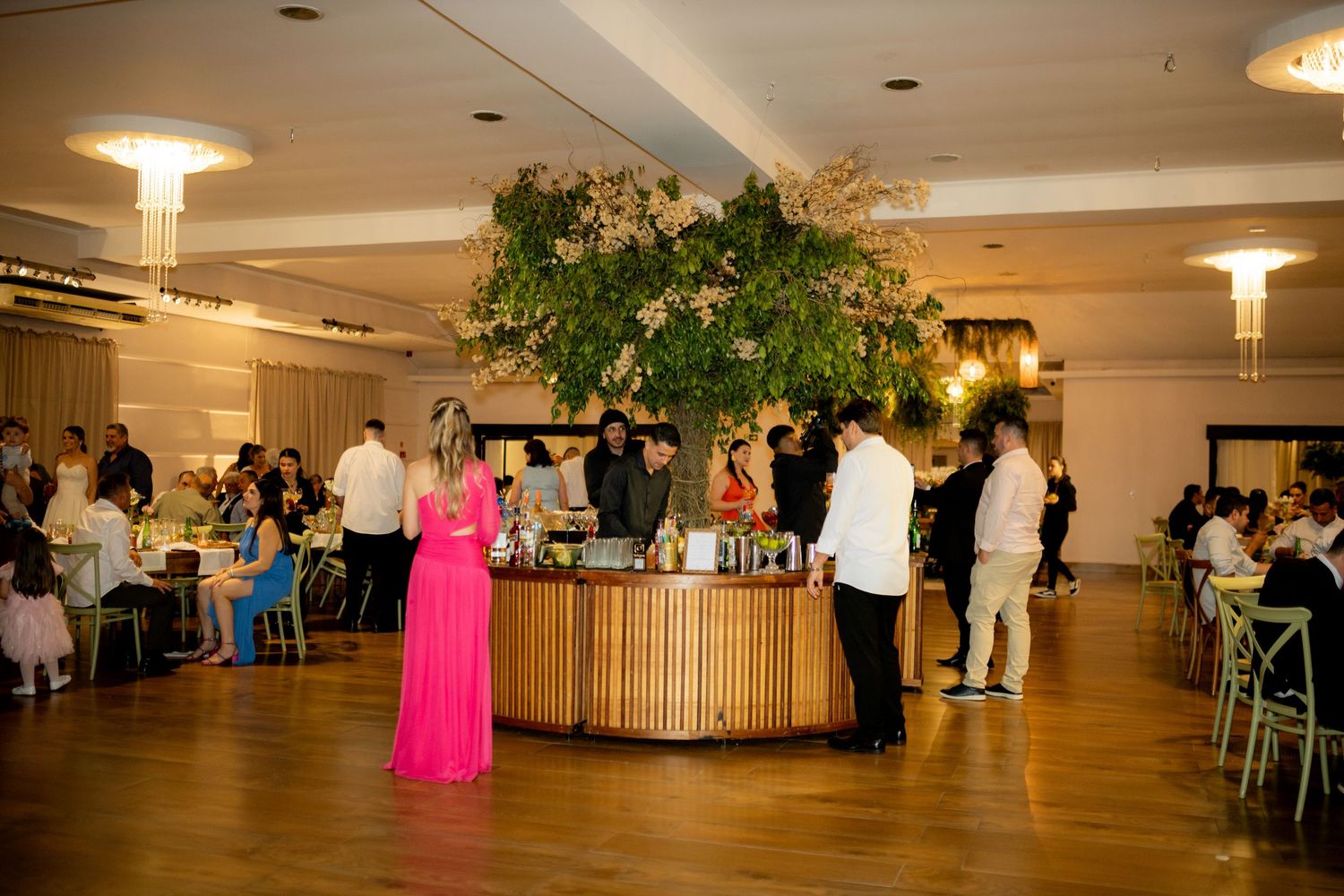 Elegant wedding reception with circular bar, lush floral centerpiece, and guests in formal attire in a grand ballroom.