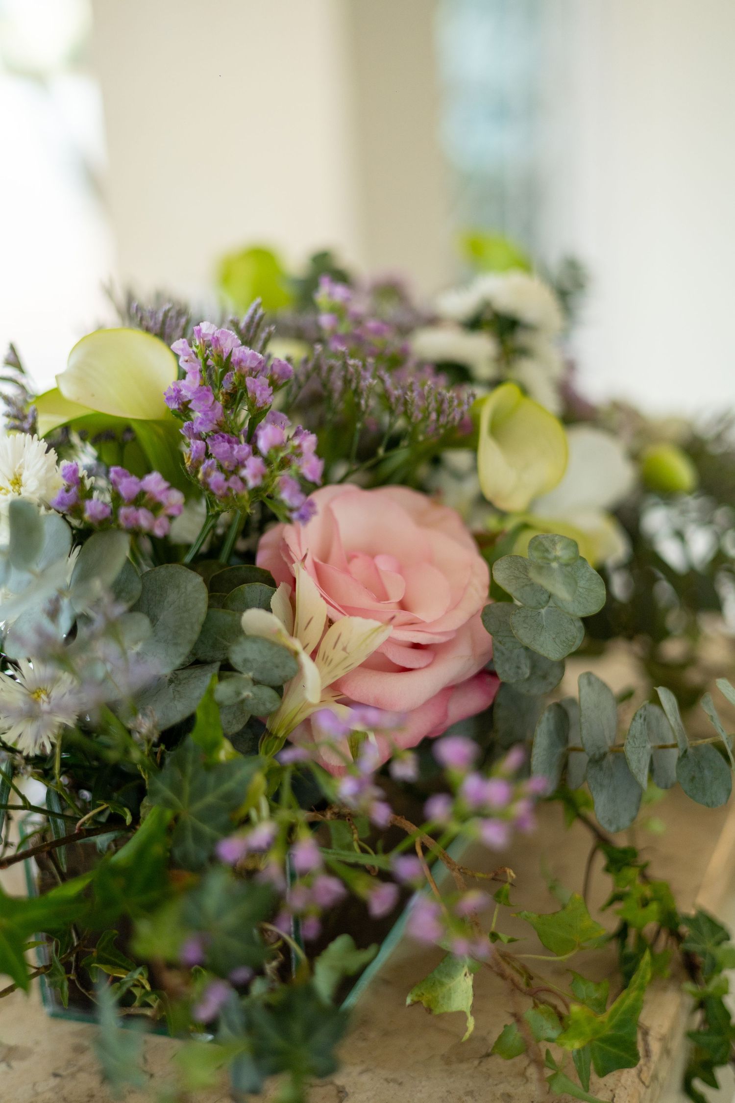Elegant floral bouquet featuring a pink rose, purple wildflowers, white calla lilies, and eucalyptus greenery on a marble surface.