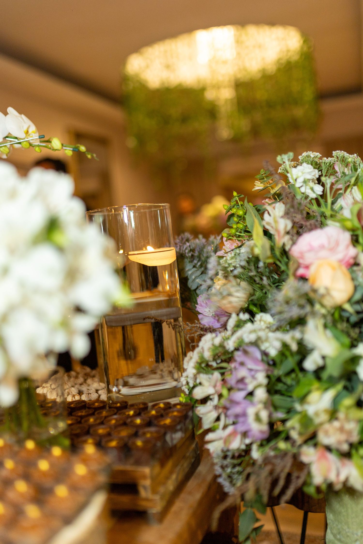 Elegant wedding reception table with floral arrangements, candles, and decorative gold boxes under warm lighting.